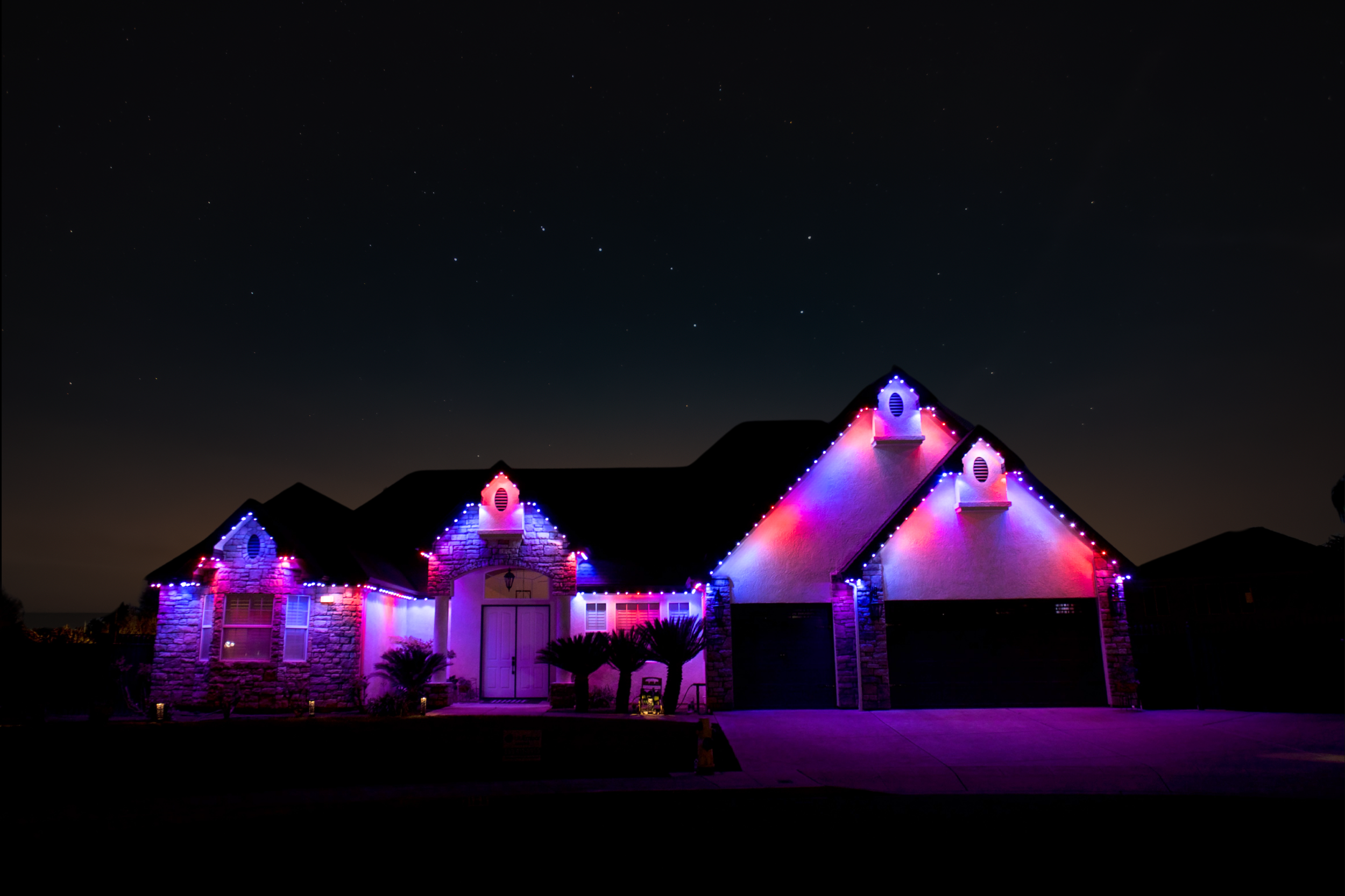 House decorated with colorful Christmas lights at night, under a starry sky.