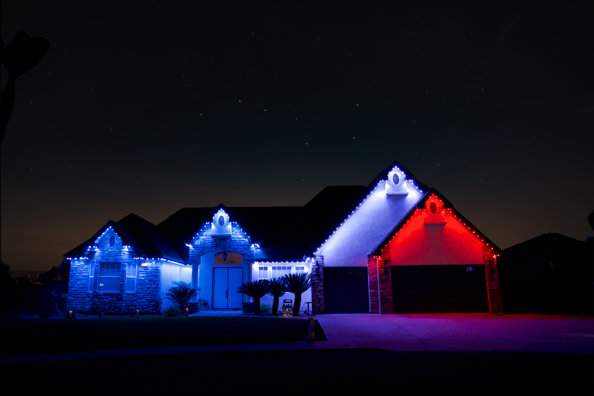 A house decorated with Christmas lights, illuminated in red, white, and blue, under a starry night sky.
