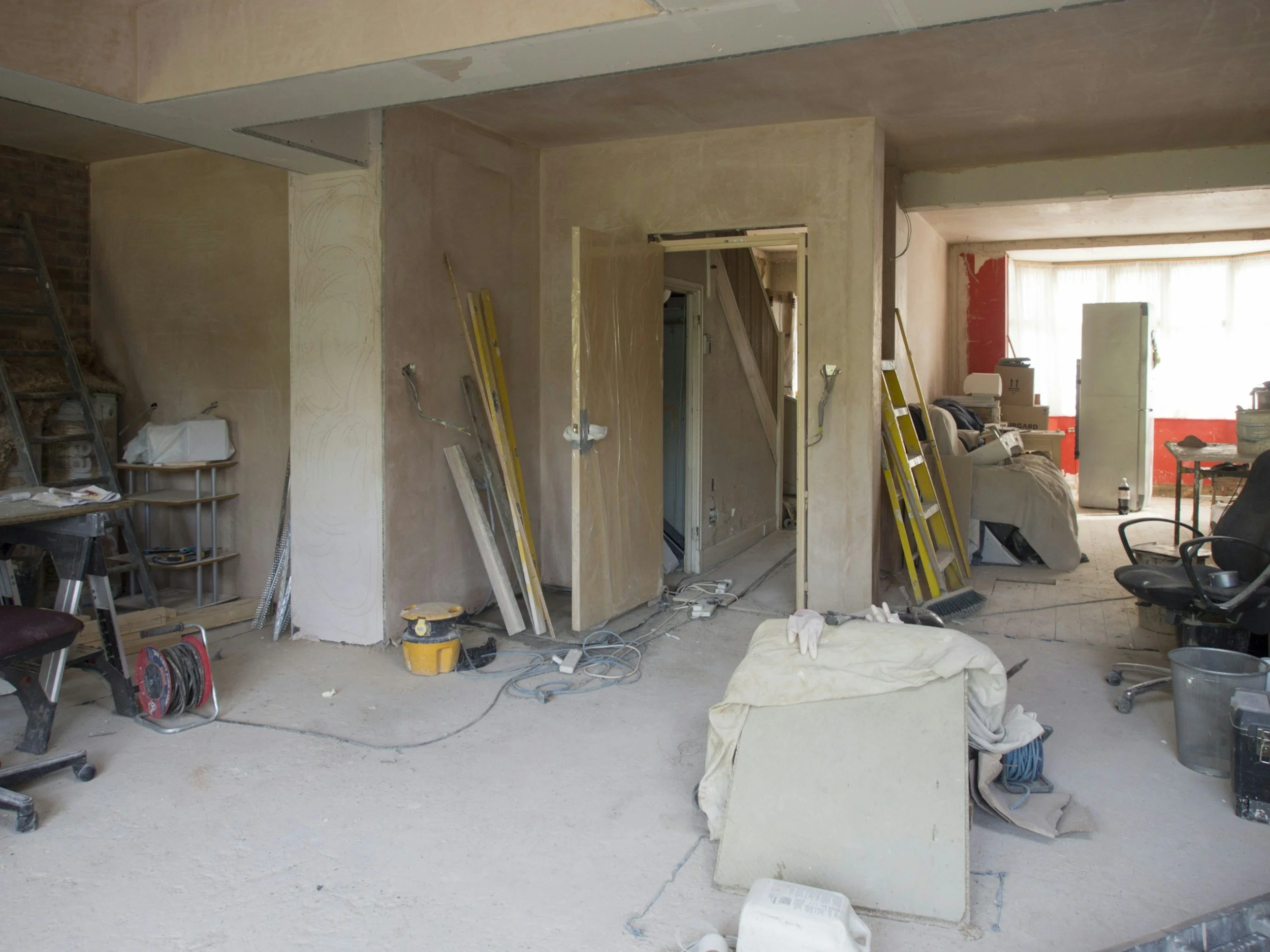 Interior of a home undergoing renovation with unfinished walls, construction tools, and materials scattered around.