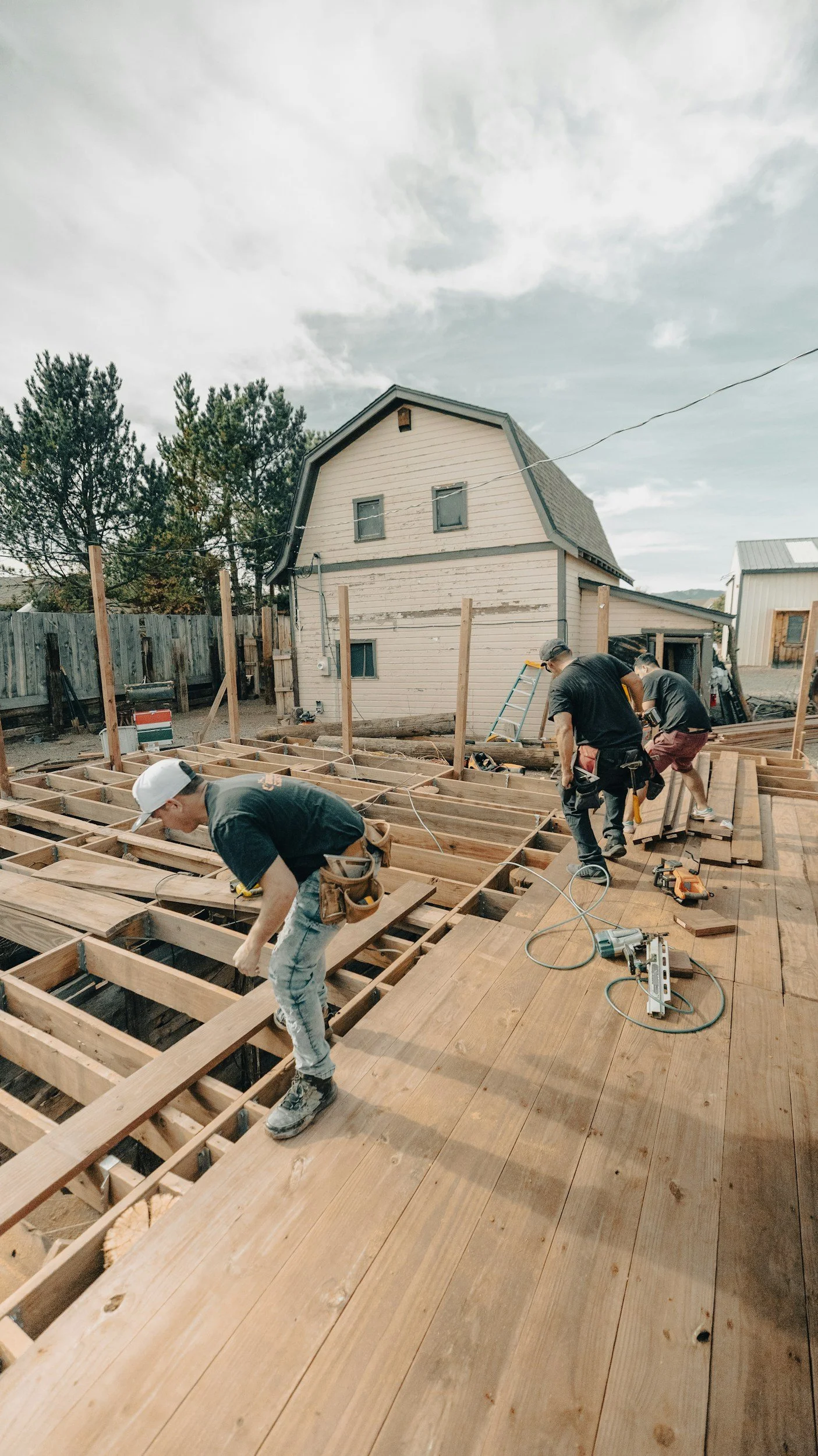 Construction workers building a wooden deck or floor outside a house on a sunny day.