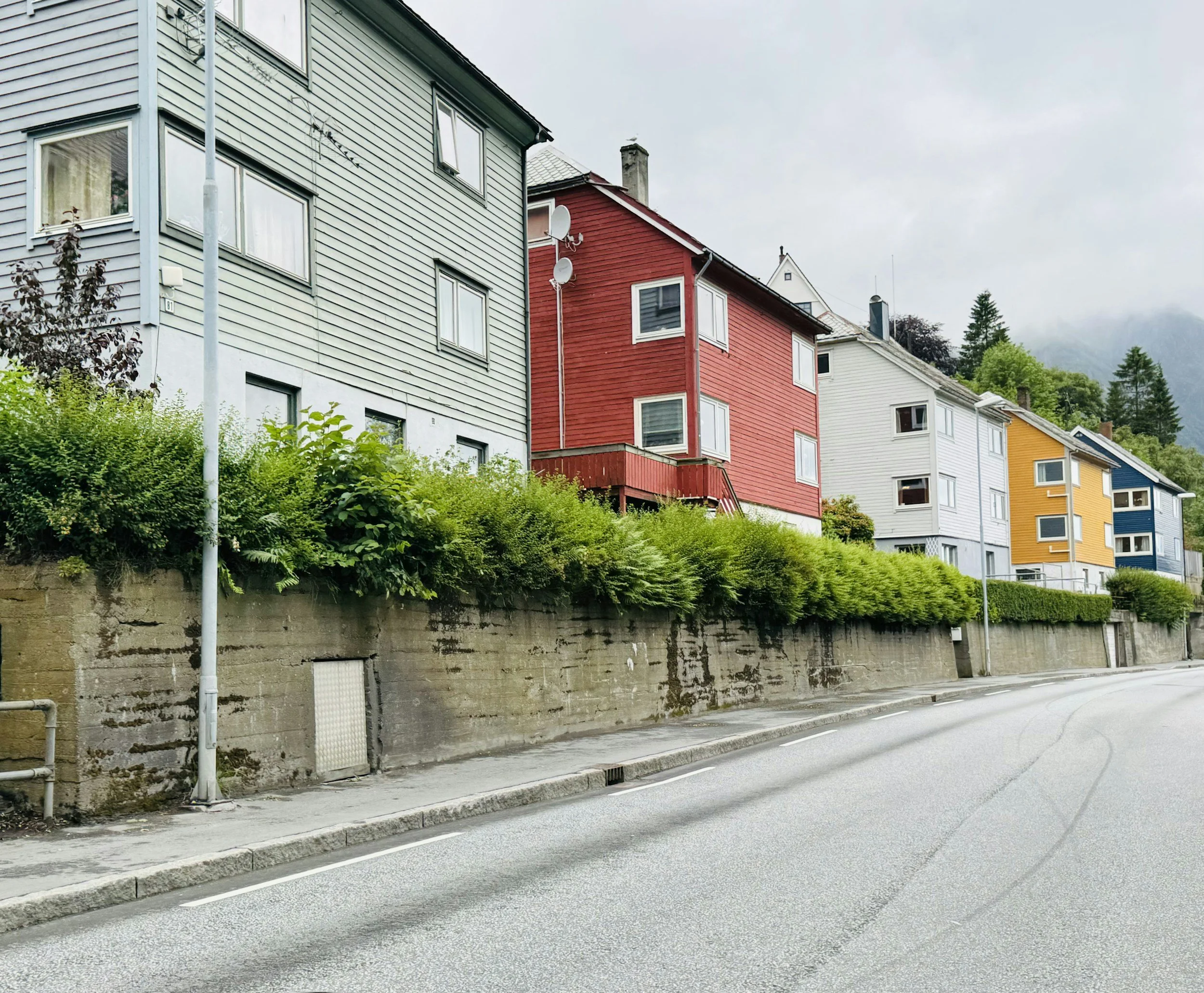 Colorful row of houses with different colored exteriors including white, yellow, red, blue, and gray, situated on a hillside with trees in the background.