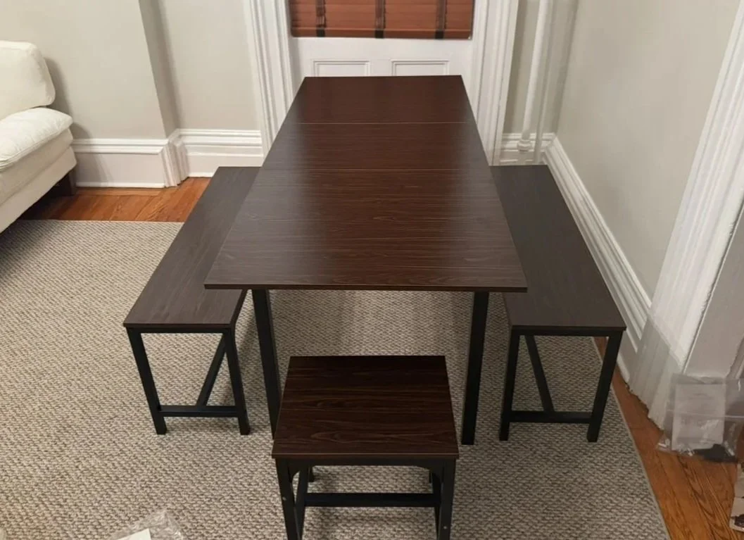 A dark wood dining table with two matching benches and a small matching stool, situated in a room with white walls, a beige carpet, and hardwood floors. Furniture Installation and Build done by Tim is Handy in Connecticut.