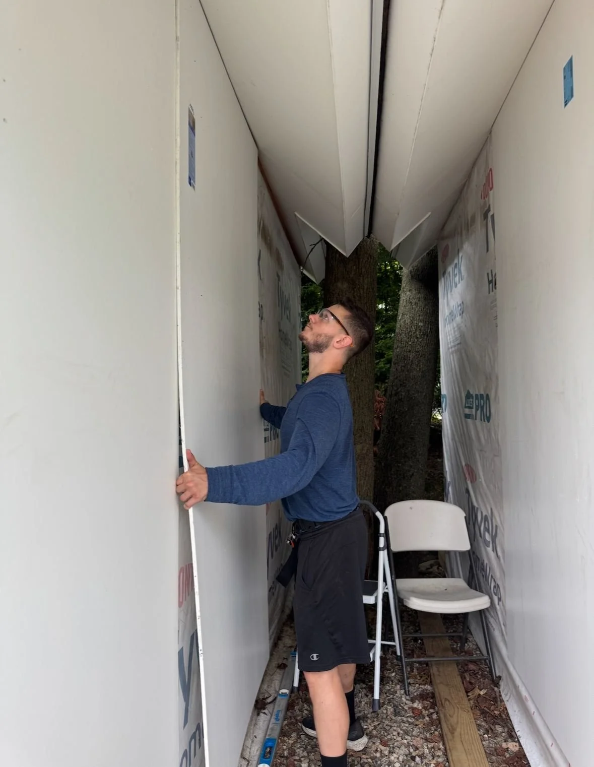 A man in a blue shirt and shorts installing siding on a small indoor structure outdoors. Tim is Handy project done in Fairfield County, CT