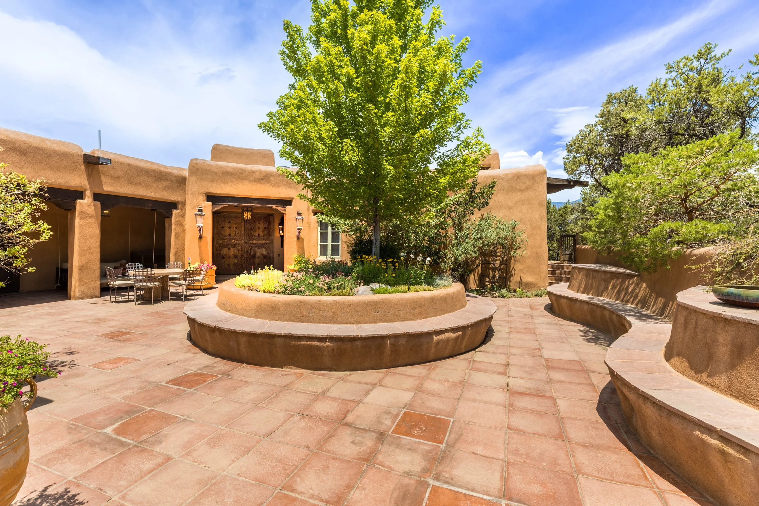 Private courtyard with mature shade tree and adobe architecture at SENDERO, a luxury estate listing by Jones West in Taos NM
