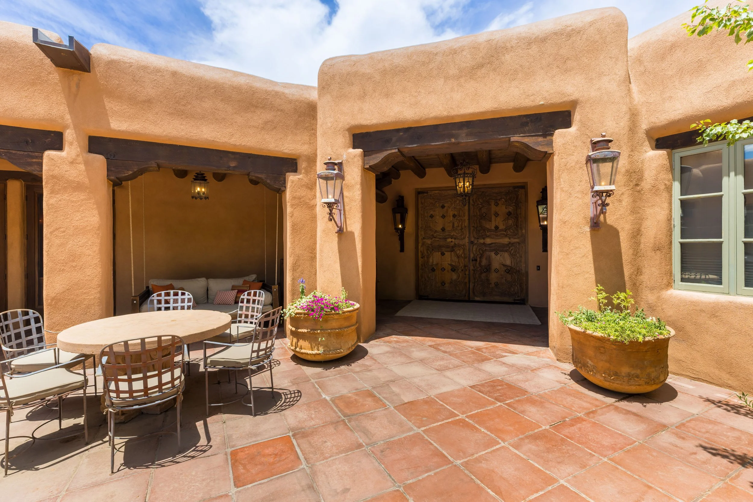 Covered portal with outdoor dining, adobe walls, and wooden vigas at SENDERO luxury estate Taos NM