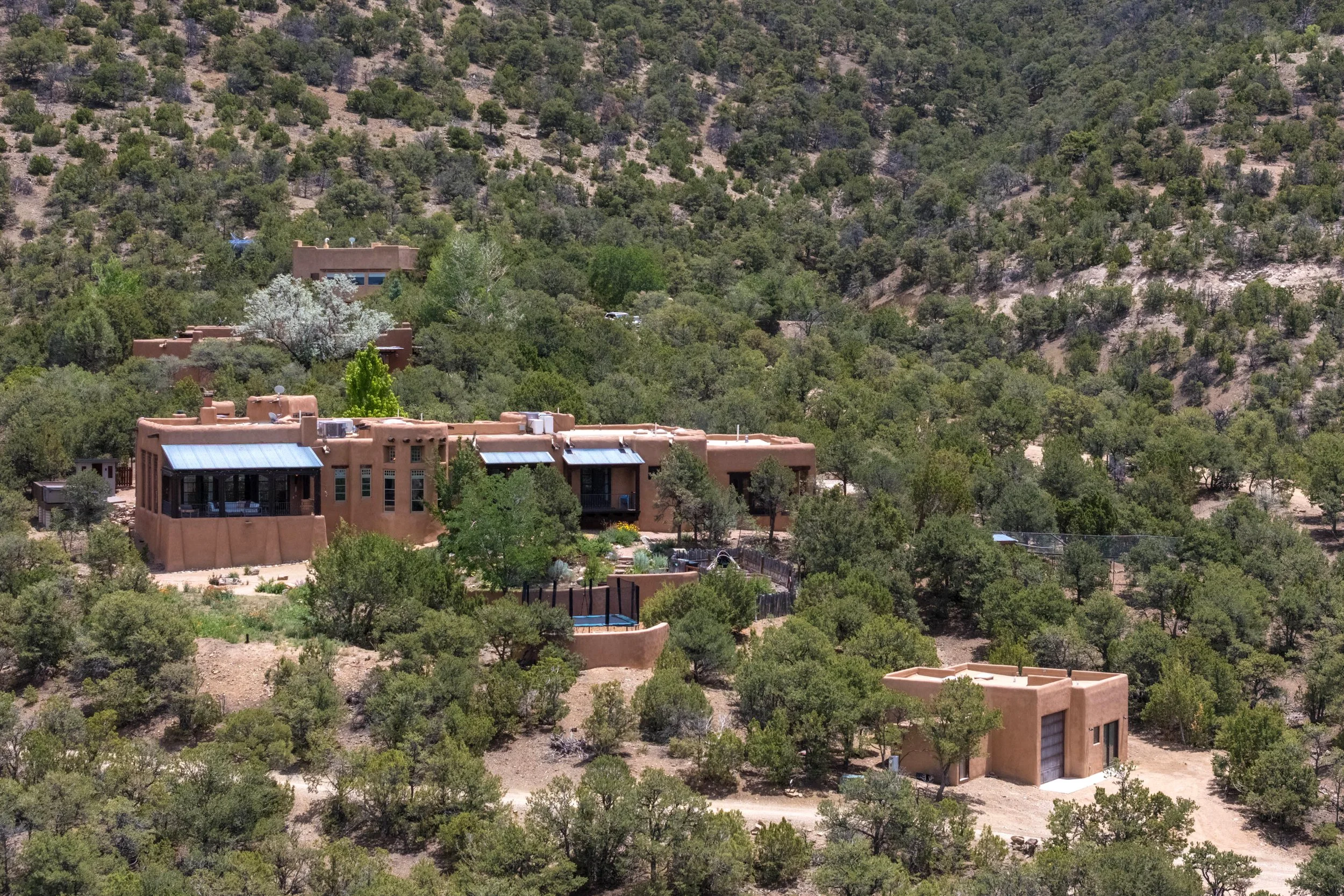 Aerial view of SENDERO multi-structure adobe compound set in pinon-juniper hillside, Taos NM — listed by Jones West