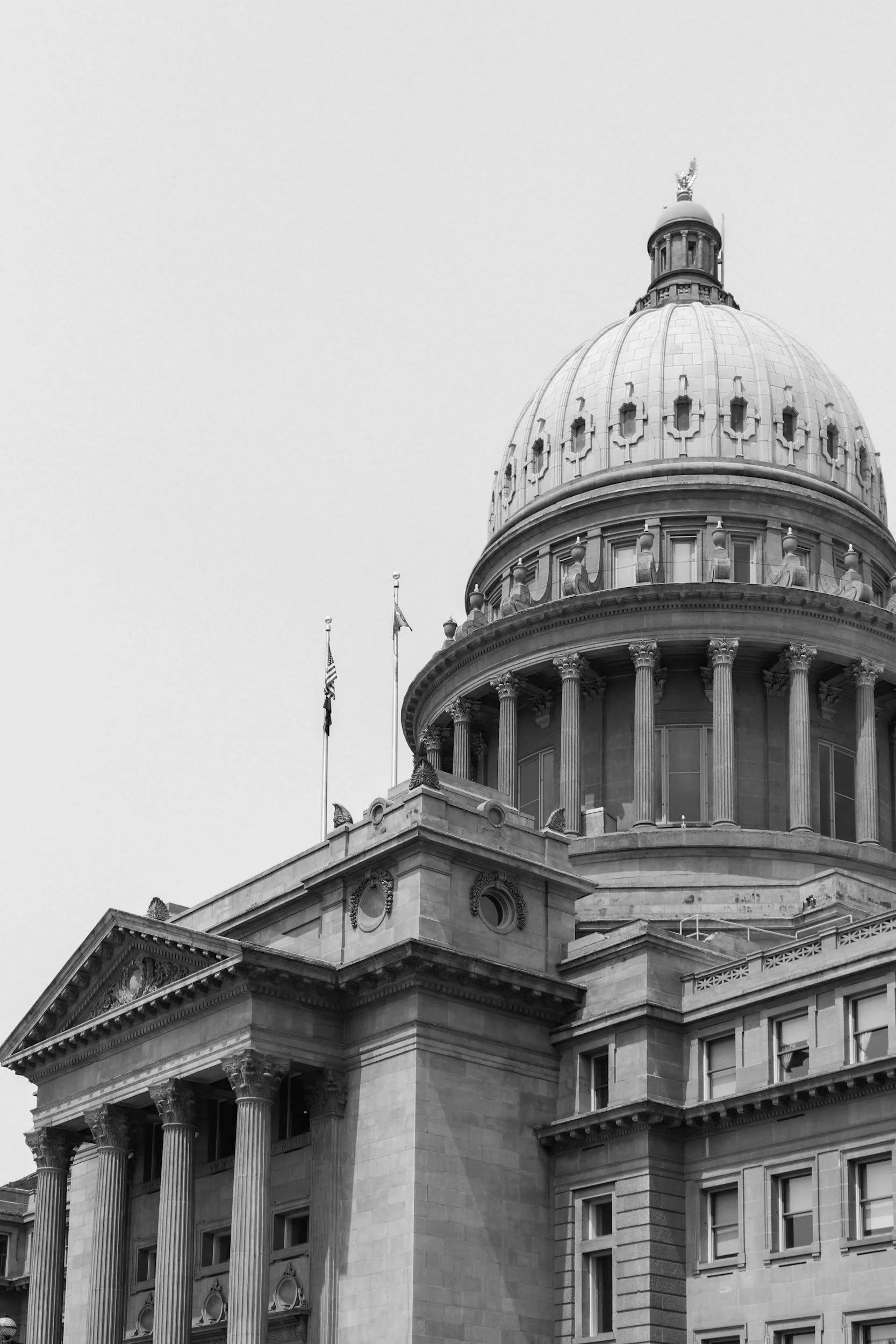 Black and white photograph of a government building with a large dome, columns, and flags, likely a capitol or state house.