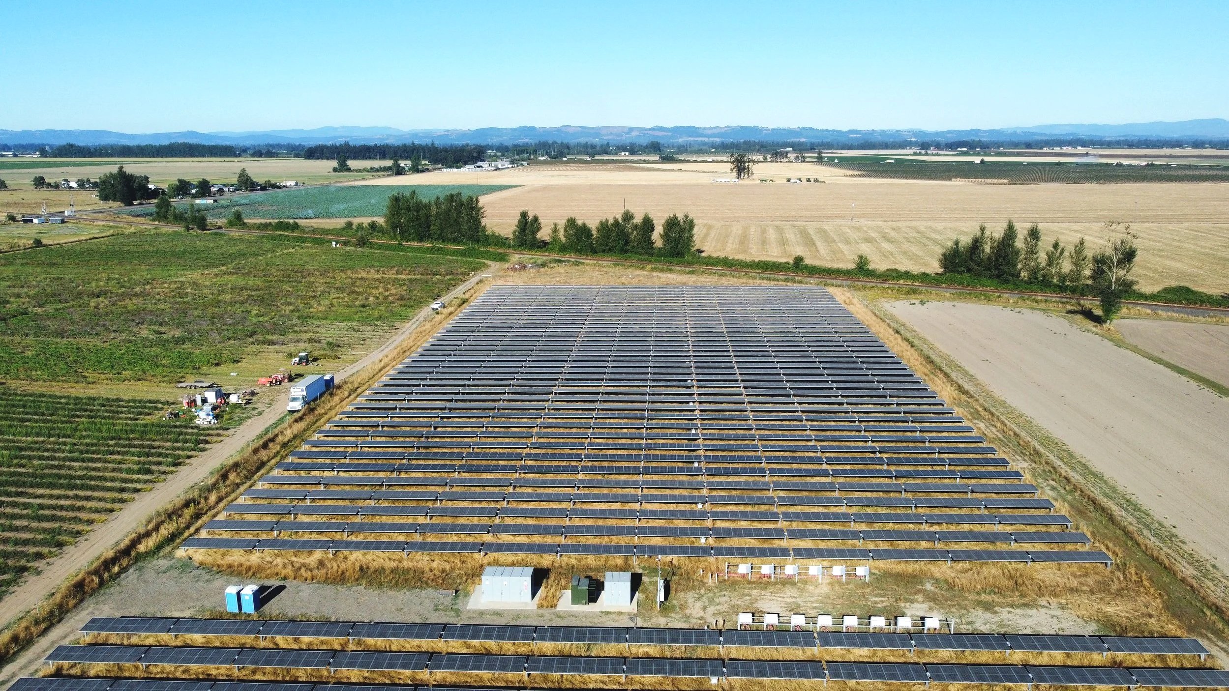 Aerial view of a solar farm with multiple rows of solar panels that has left ample room for farming around it under a clear blue sky.