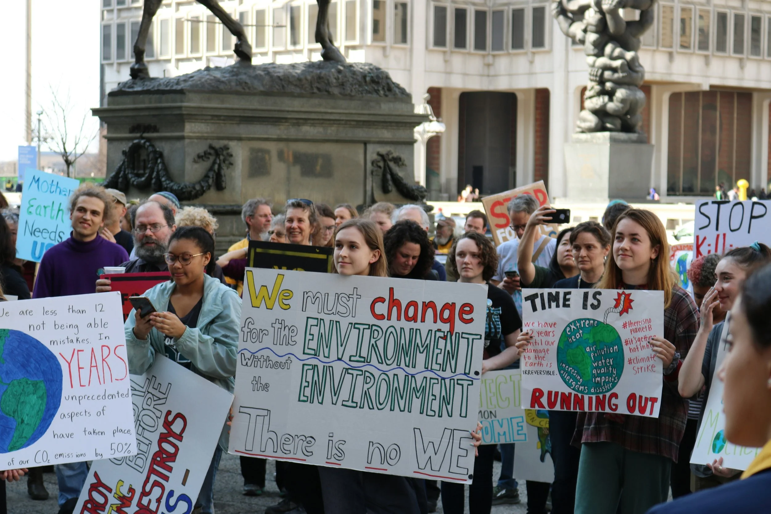 A crowd of people participating in an environmental protest, holding various signs advocating for climate action and environmental protection.