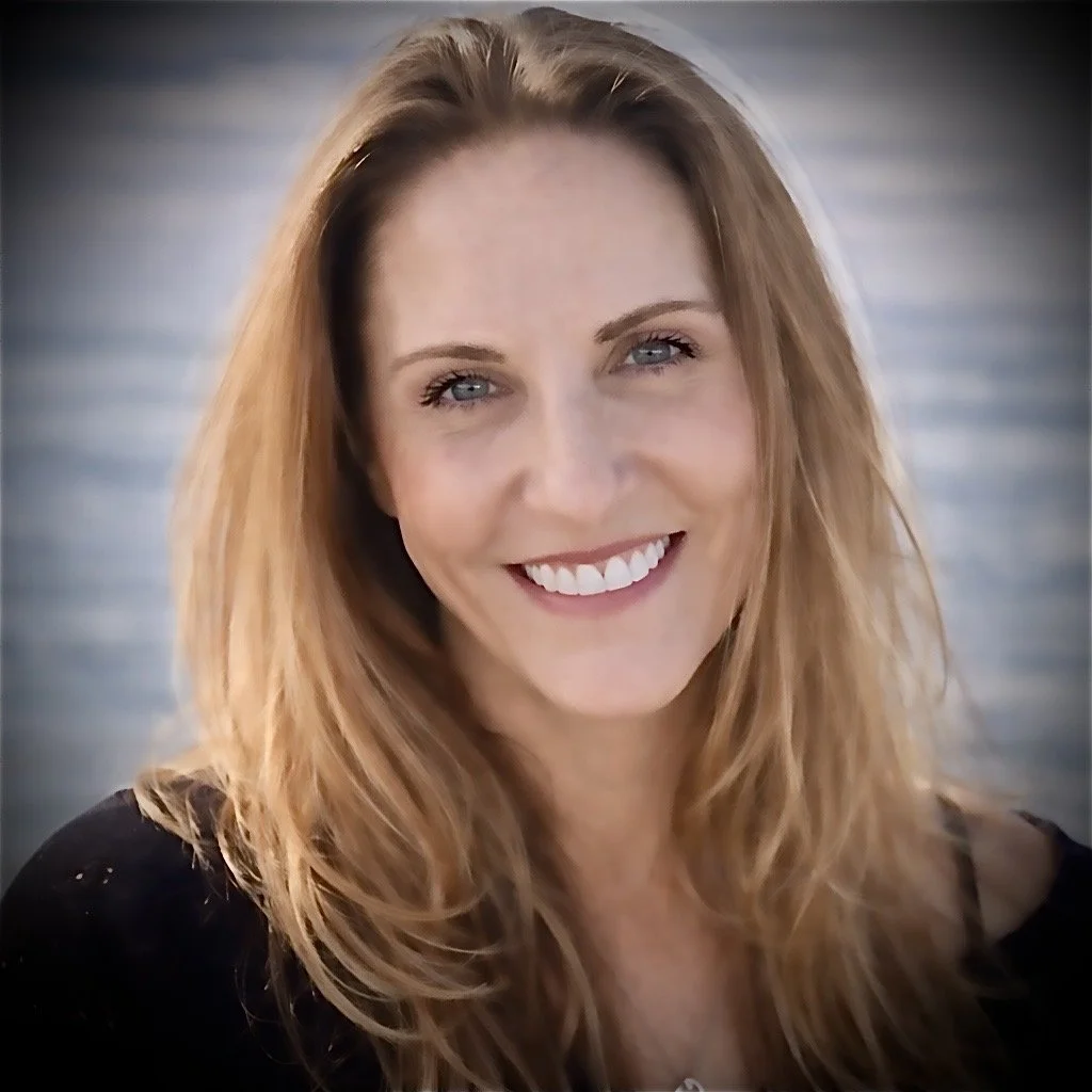 A woman with long, wavy red hair and blue eyes smiling at the camera.