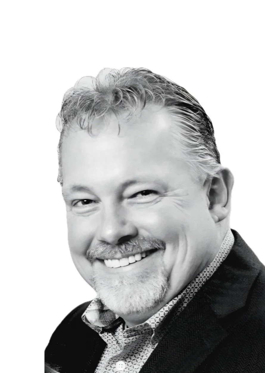 Black and white portrait of a smiling man with a goatee, wearing a suit jacket and a patterned shirt.