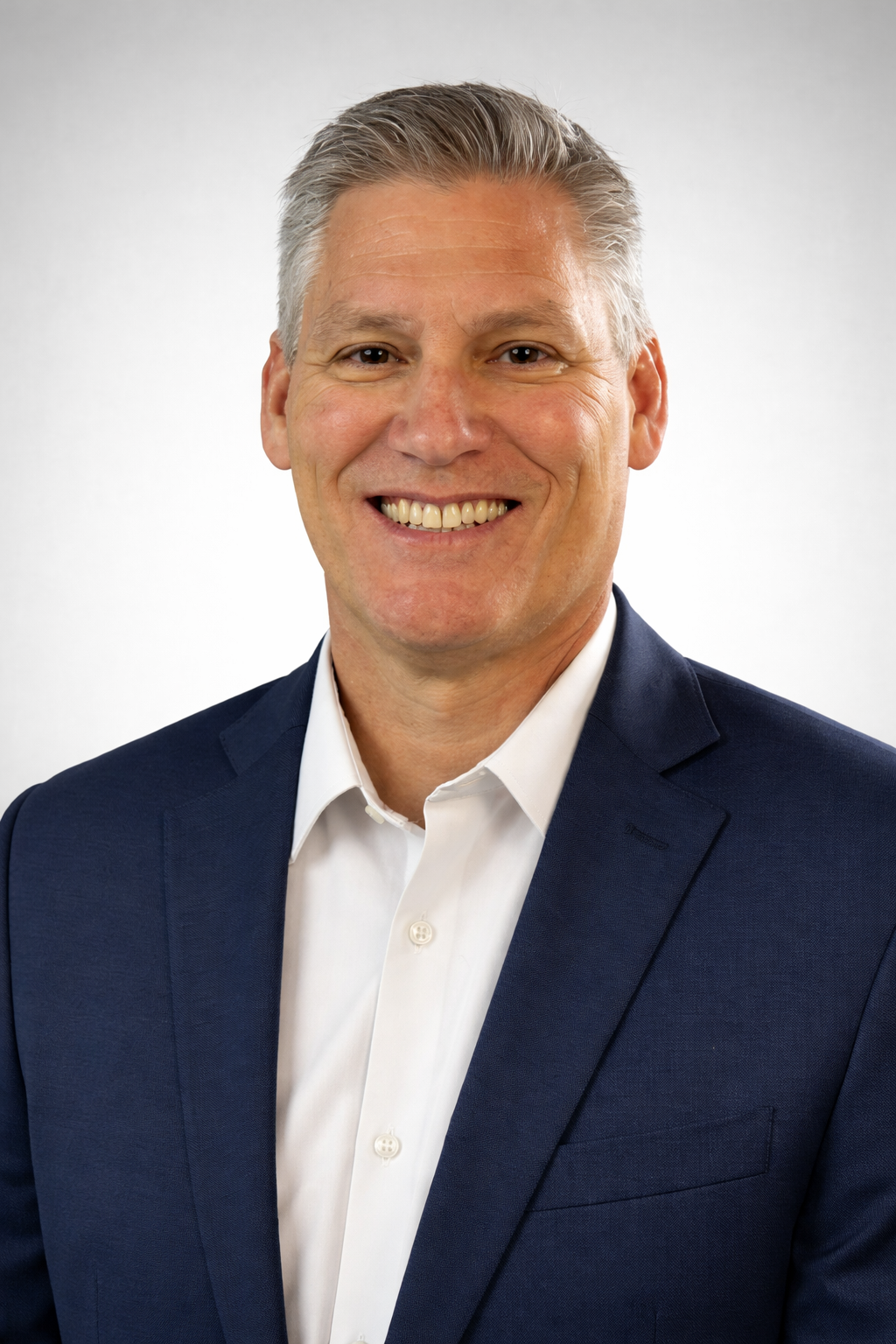 Smiling middle-aged man with graying hair in a navy blue suit and white shirt, posing against a plain white background.