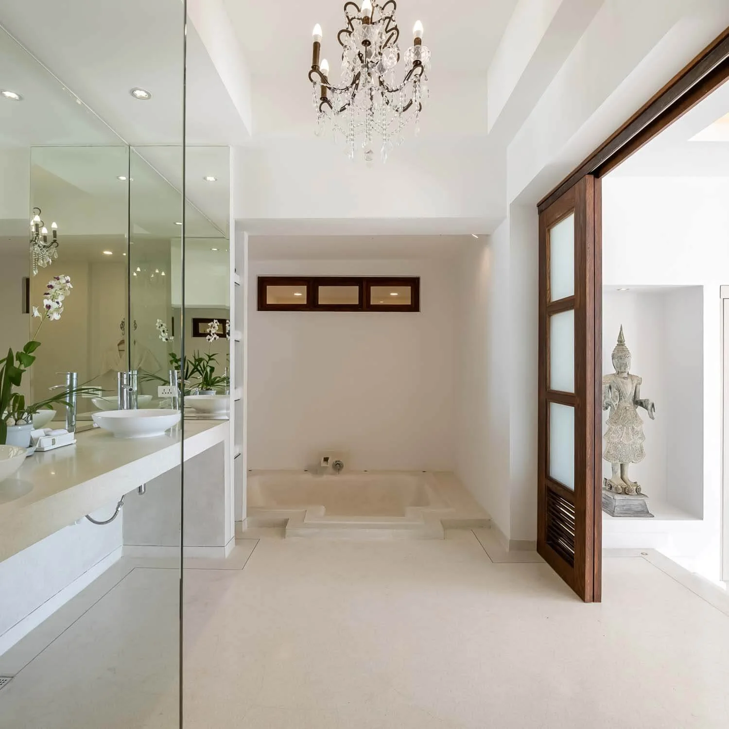 Luxury en-suite bathroom with a crystal chandelier, deep soaking tub, double vanity mirrors, and a traditional Thai Buddha statue at Saensook eco villa