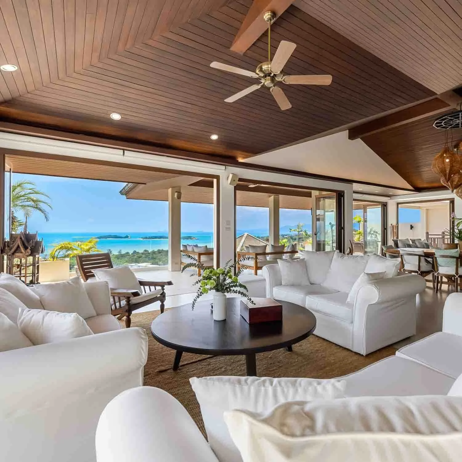 Open-plan luxury living at Saensook in Koh Samui featuring plush white sofas, vaulted wooden ceilings, and seamless indoor-outdoor tropical views.
