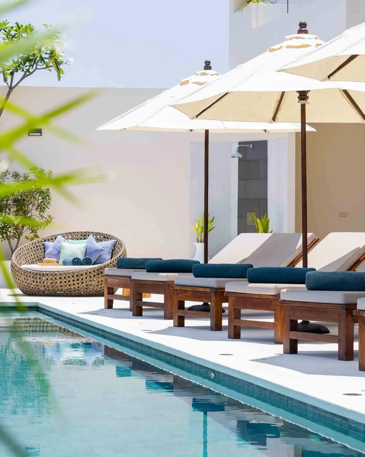 Sun loungers with white umbrellas and a round rattan daybed lined up along the pristine pool deck at Saensook eco villa