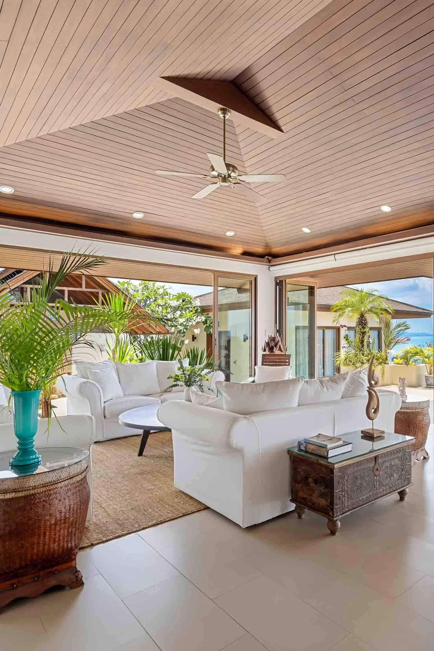 Spacious open-plan living room with white sofas, a vaulted wooden ceiling, and sliding glass doors opening to panoramic sea views at Saensook villa