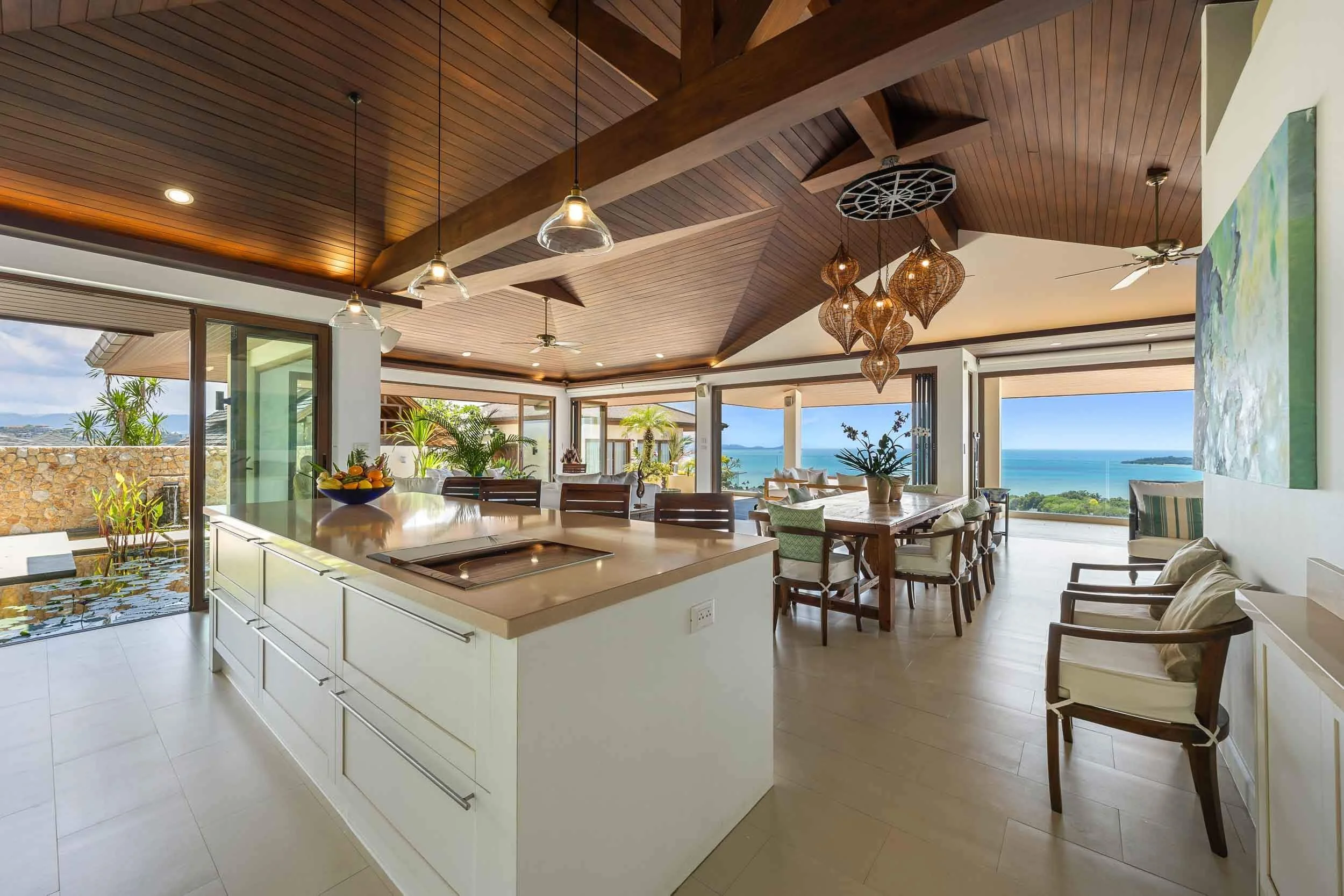 Modern luxury kitchen at Saensook Villa featuring a large central island, warm wooden vaulted ceilings, and an adjoining dining space with ocean views.
