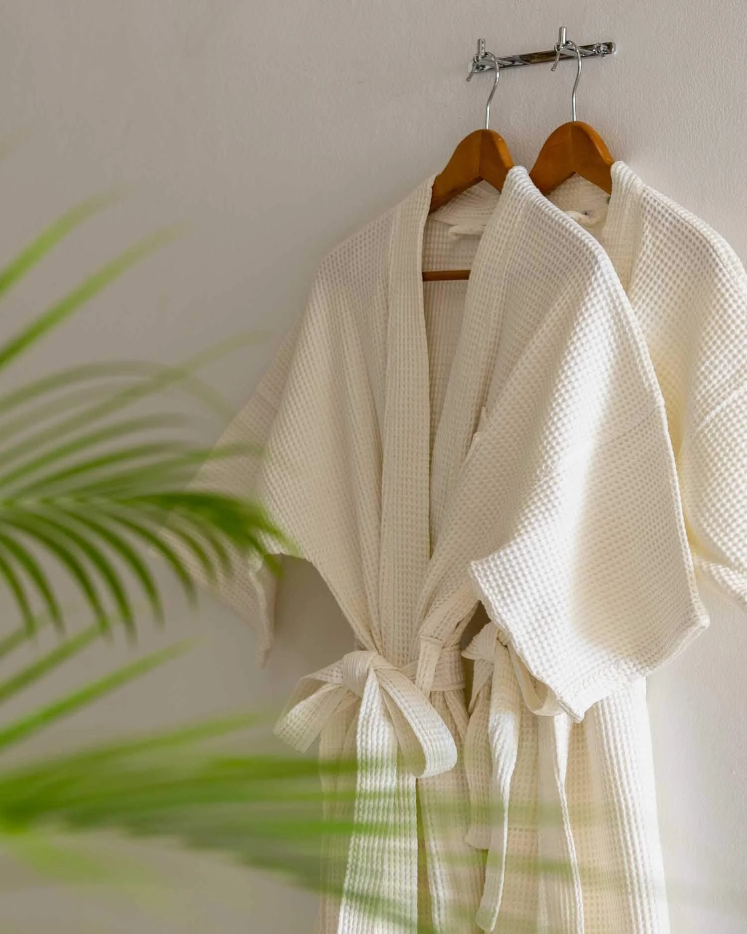 Fluffy white waffle-weave bathrobes hanging neatly on wooden hangers, representing luxury bathroom amenities at Saensook eco villa, Koh Samui