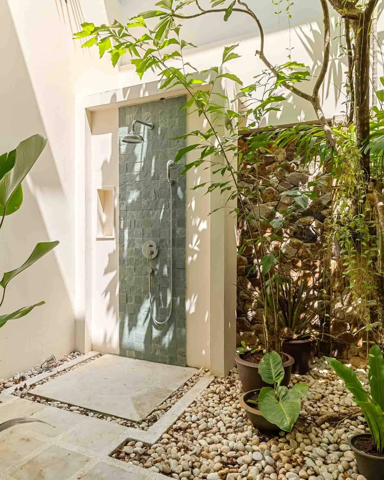 Open-air tropical stone shower surrounded by greenery in the private en-suite bathroom of the Sundown Suite at Saensook villa