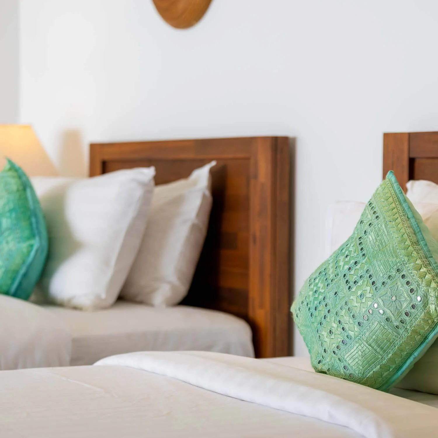 A bedroom with two beds, each with white pillows and green decorative pillows, wooden headboards, and a white wall in the background.
