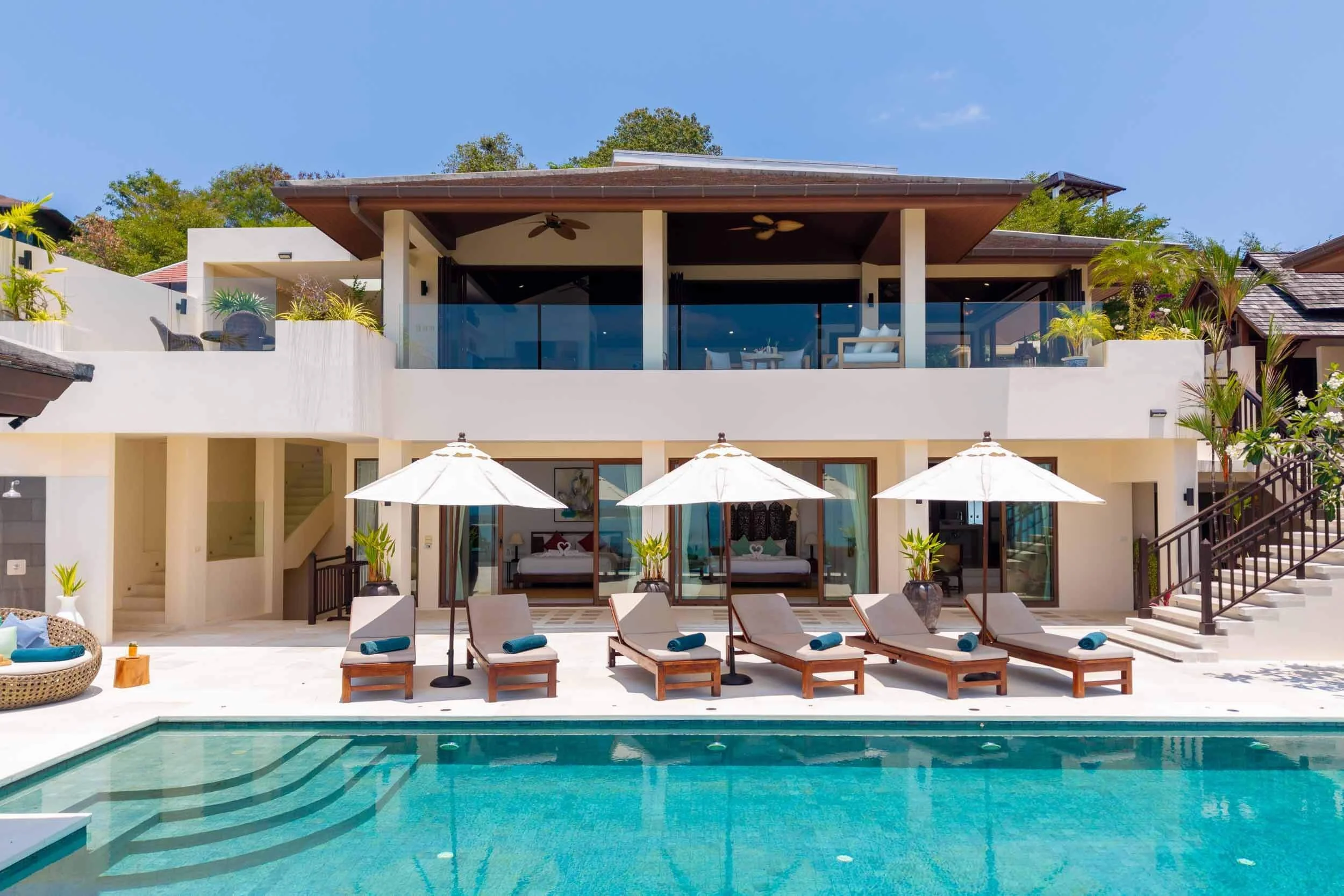 Sunlit poolside patio of Saensook Villa with lounge chairs, white umbrellas, and direct access to the ground-floor suites.