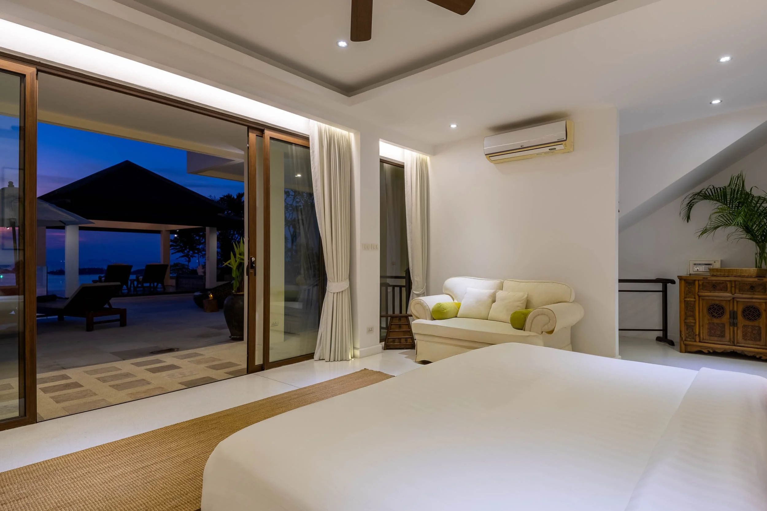 Sanctuary Suite bedroom at dusk, featuring a king bed and open sliding glass doors looking out to a dramatic twilight sky and the villa's pool deck