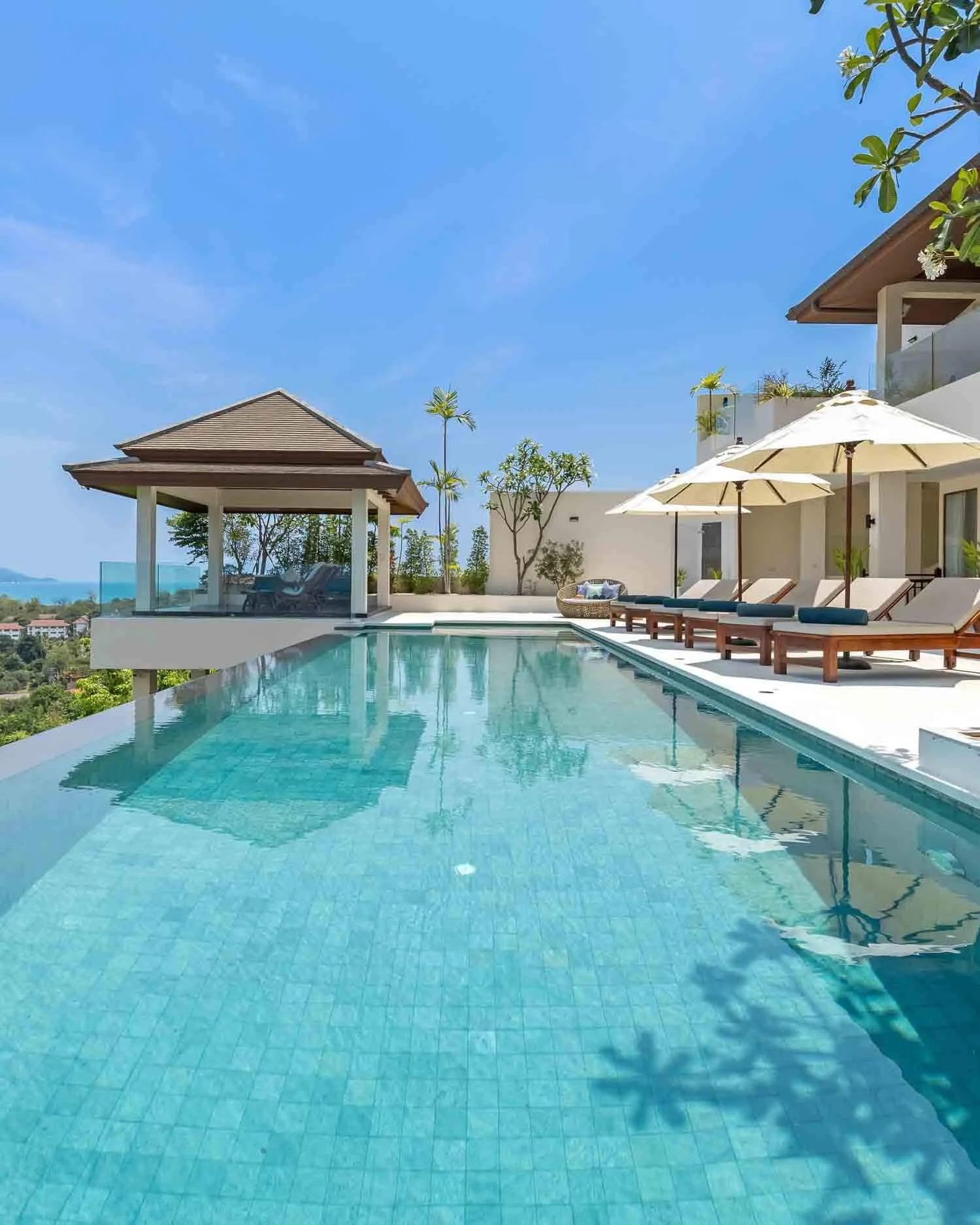 Infinity swimming pool with sun loungers and a traditional Thai pavilion at Saensook Villa overlooking the lush tropical landscape and sea.