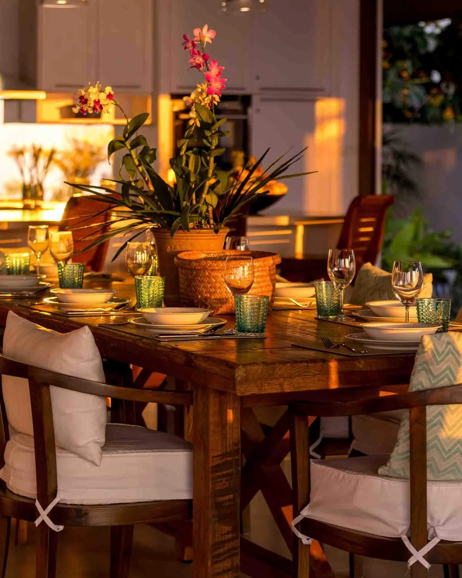 A rustic wooden dining table beautifully set with wine glasses, white dishware, and vibrant orchids, illuminated by golden sunset light at Saensook eco villa