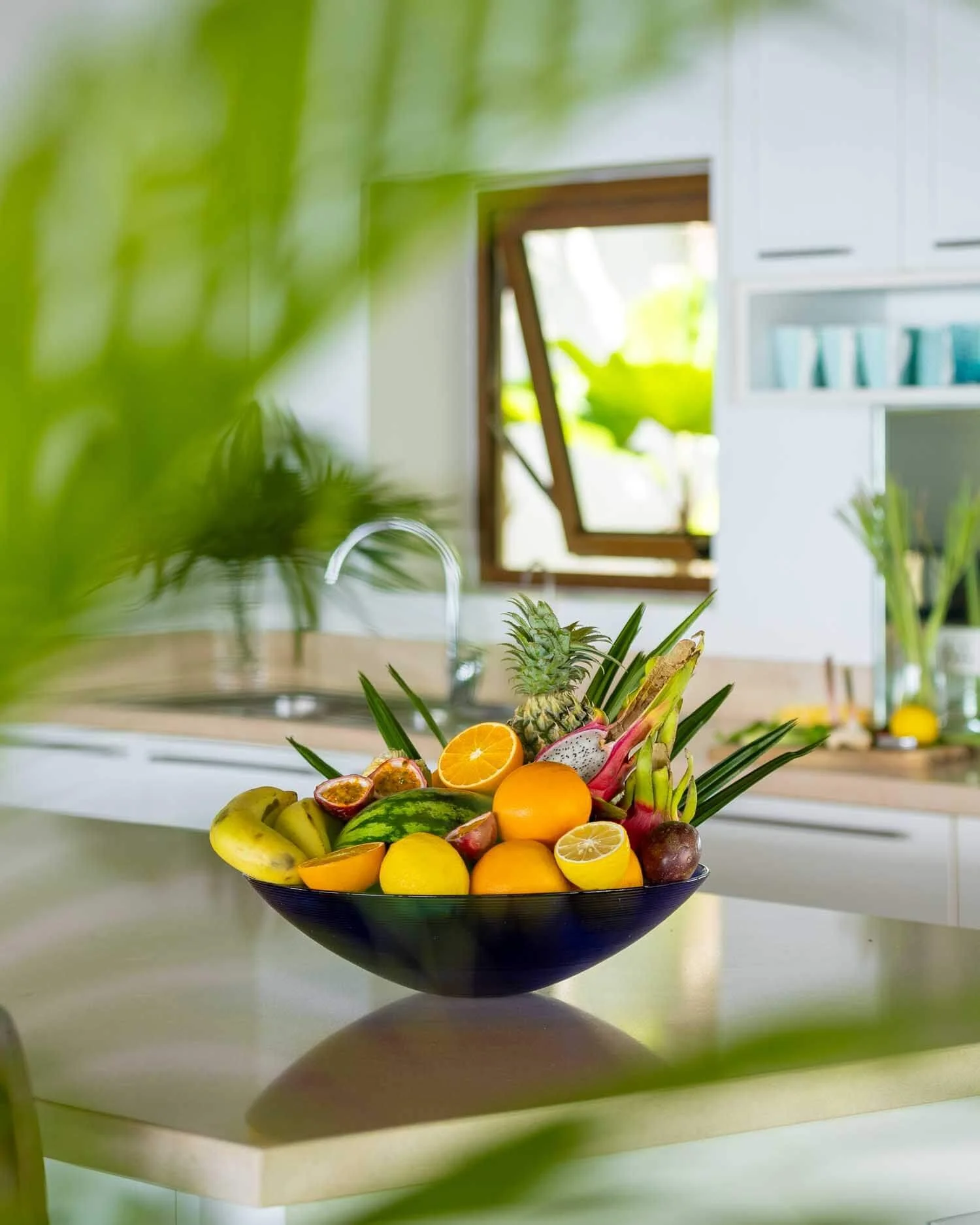 A large glass bowl filled with fresh tropical fruit, including a pineapple, bananas, and citrus, resting on a kitchen counter at Saensook villa