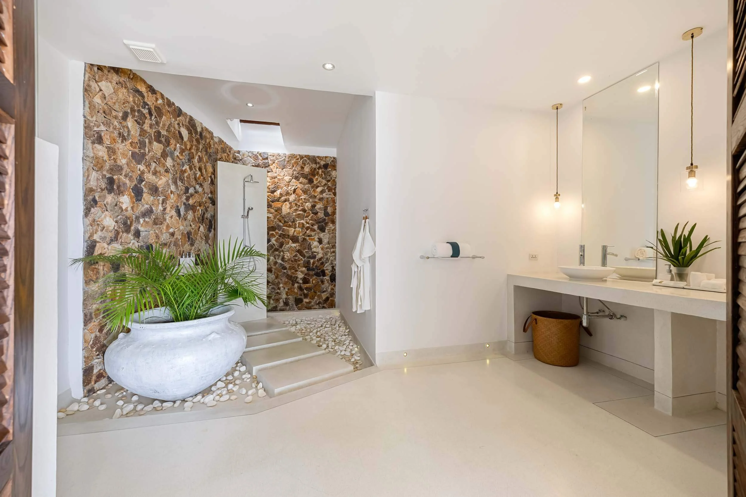 Luxury eco-friendly en-suite bathroom in the Sanctuary Suite, featuring a stone feature wall, rainfall shower over smooth pebbles, and a double vanity