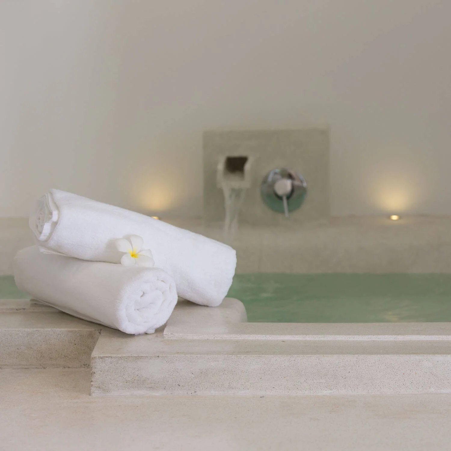 Rolled white spa towels with a frangipani flower resting on the edge of a luxury sunken bathtub at Saensook eco villa