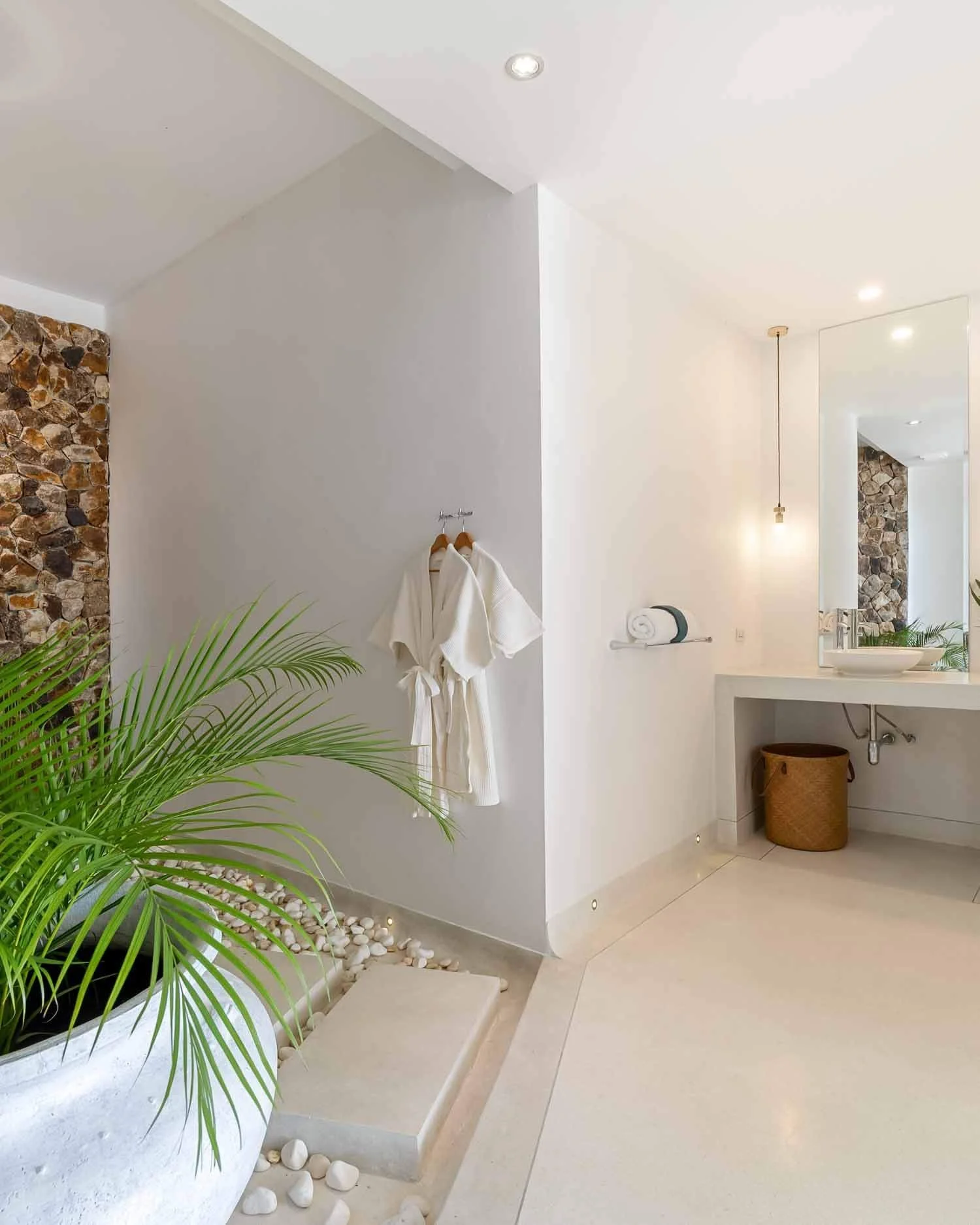 Close-up view of the minimalist white vanity, hanging robes, and indoor greenery in the open-air style bathroom of the Sanctuary Suite at Saensook villa