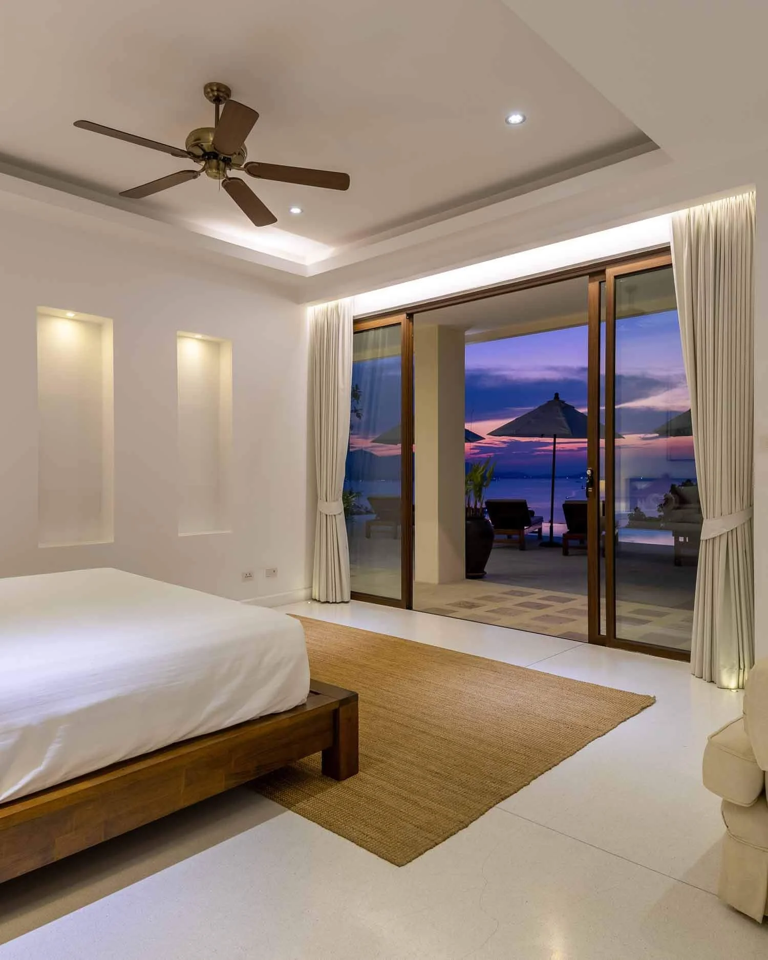 Cozy seating area and king bed inside the Sanctuary Suite, with large sliding glass doors framing a twilight view at Saensook eco villa