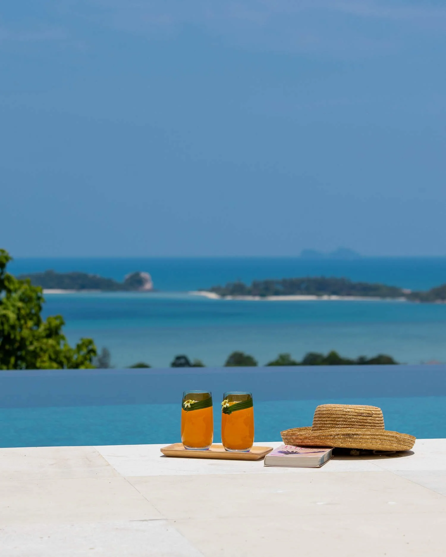 Refreshing tropical drinks and a straw hat resting on the edge of the infinity pool overlooking the blue sea near Koh Samui