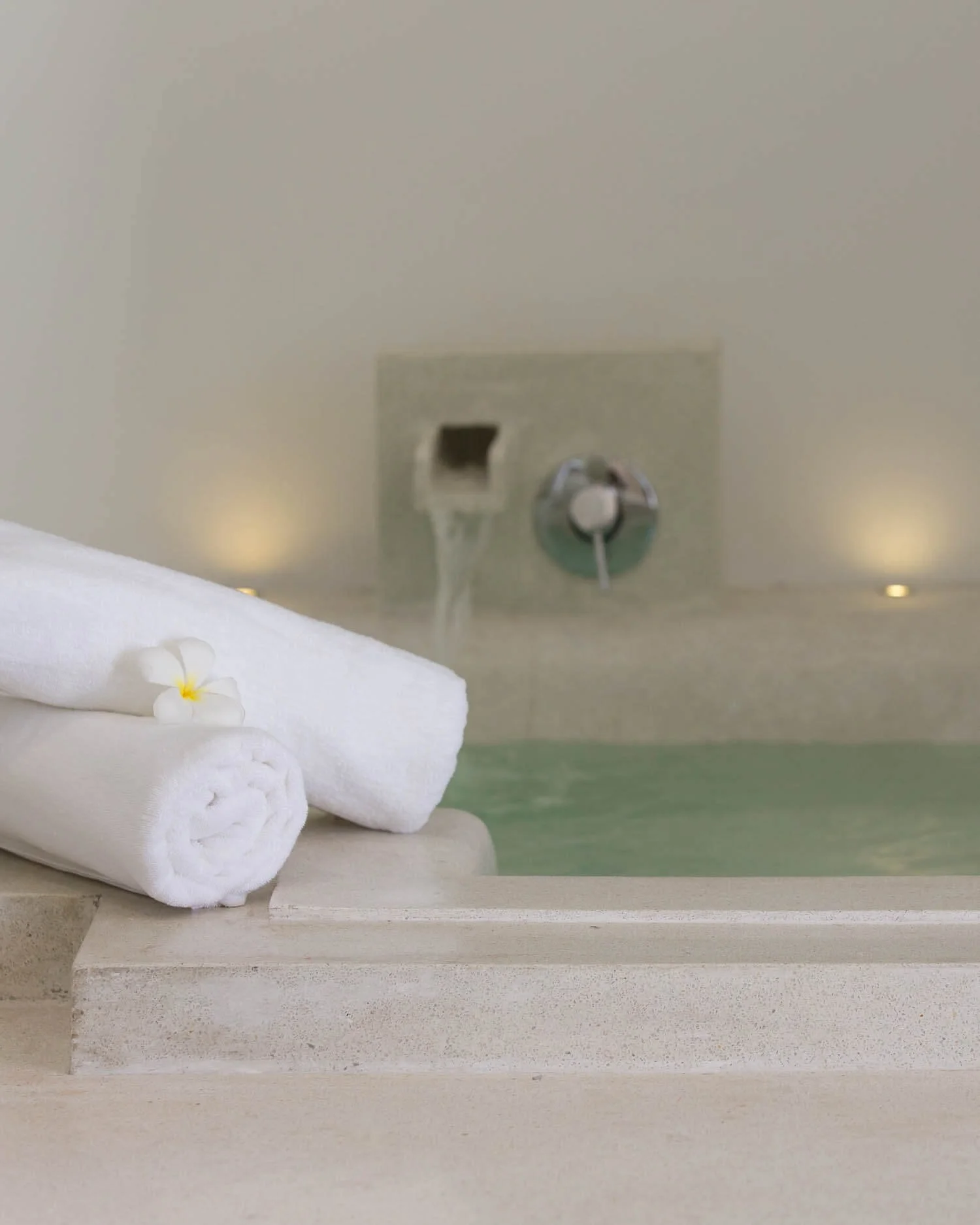 Rolled white spa towels with a frangipani flower resting on the edge of the luxury built-in soaking bathtub in the Spa Suite at Saensook villa