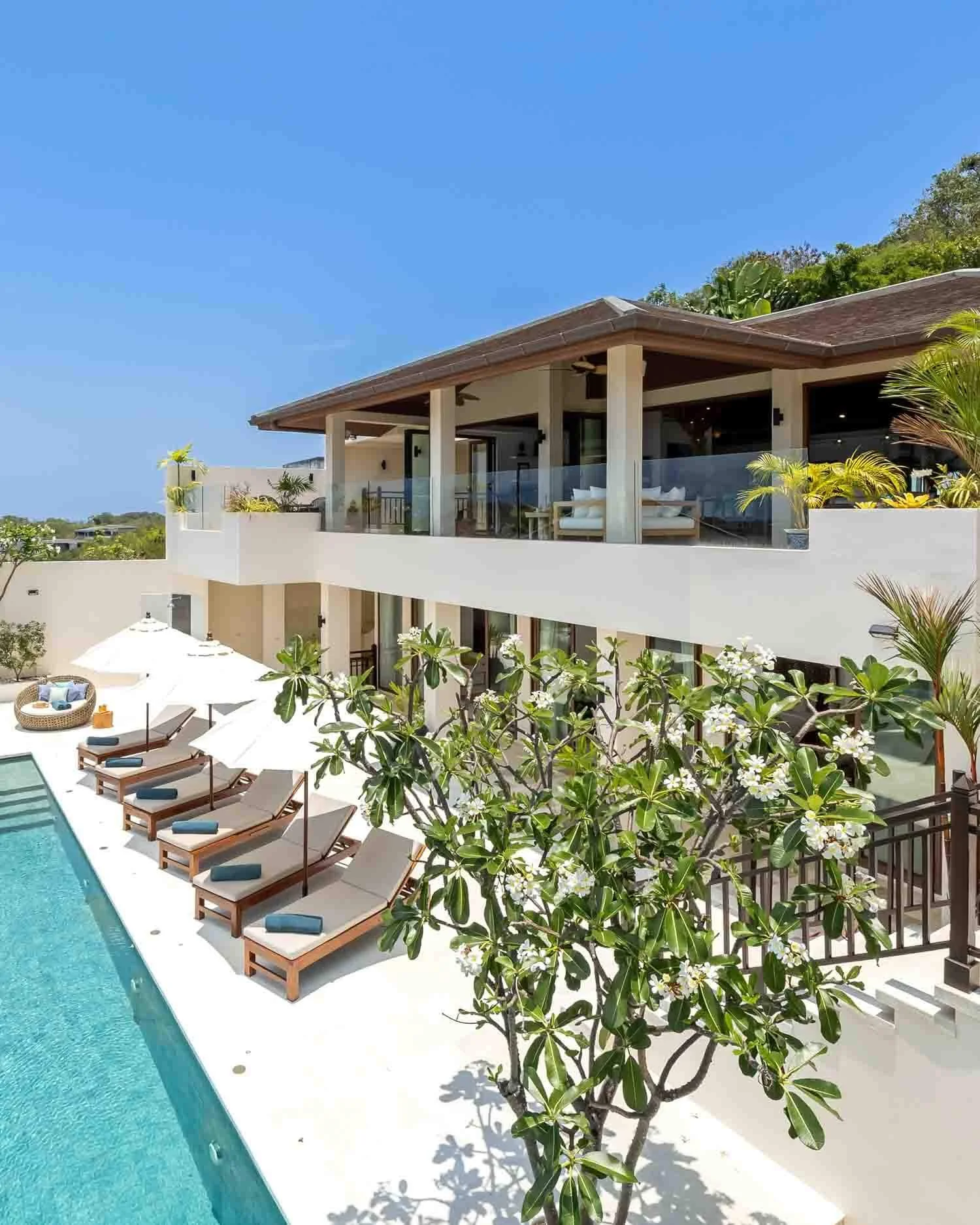 Exterior view looking up at the villa's sun deck, white sun loungers by the pool, and blooming frangipani trees at Saensook eco villa