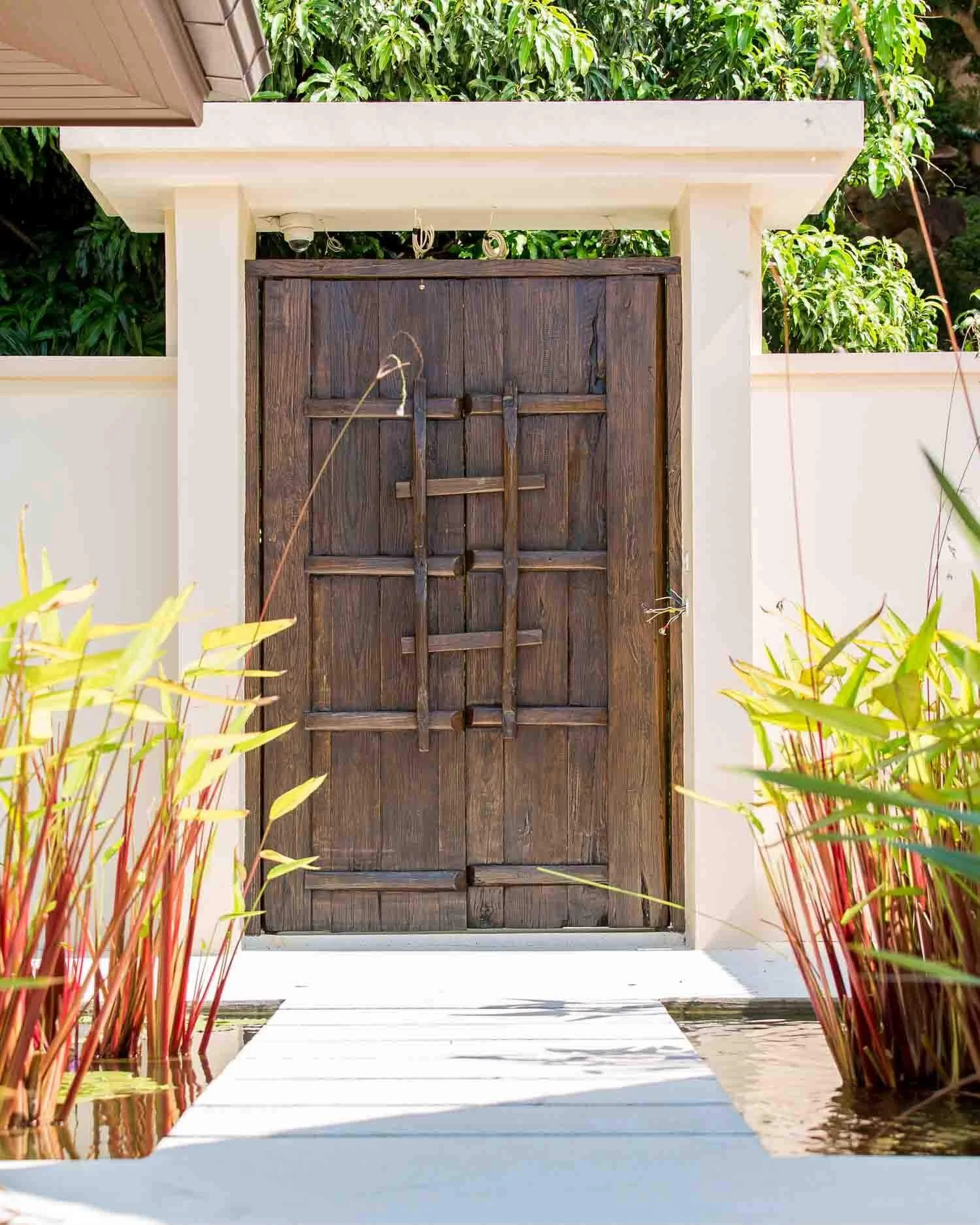 Traditional wooden entrance gate set amidst lush tropical plants and a reflective water feature at Saensook villa in Koh Samui