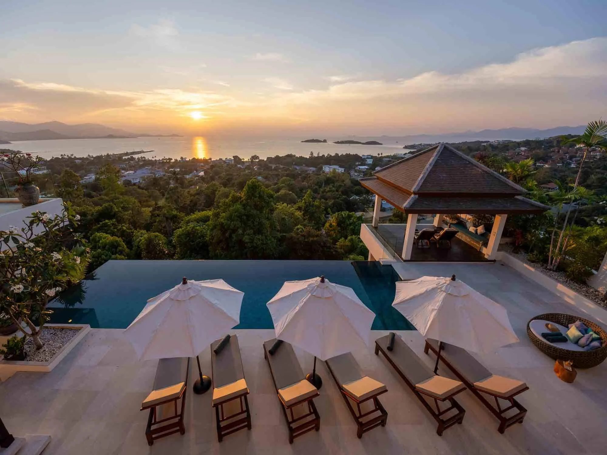 Aerial view of the stunning sunset over the infinity pool, sun loungers, umbrellas, and outdoor pavilion at Saensook eco villa in Koh Samui