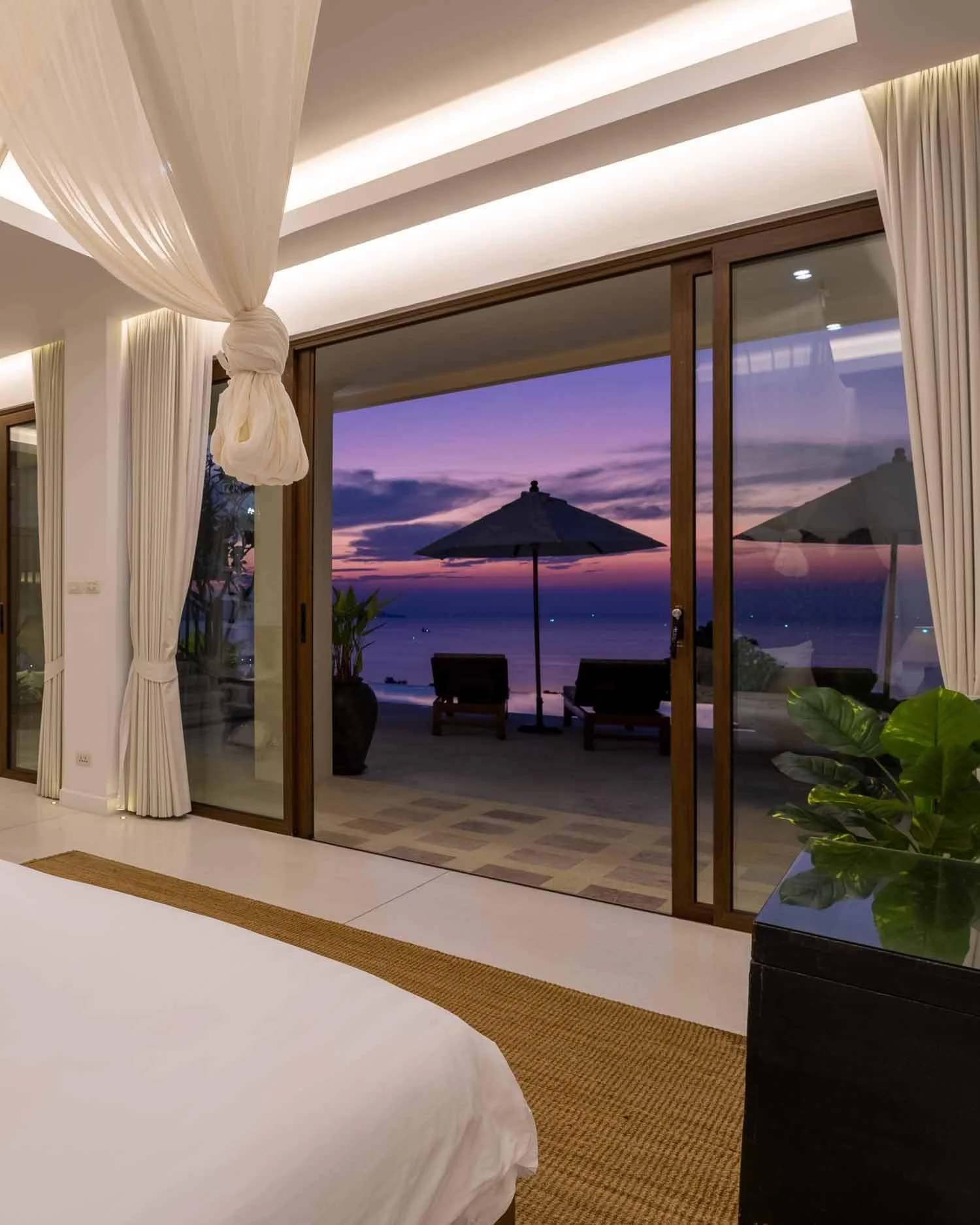 Dusk view from the bed looking through open glass sliding doors to a vibrant purple sunset sky over the sea from the Spa Suite at Saensook eco villa