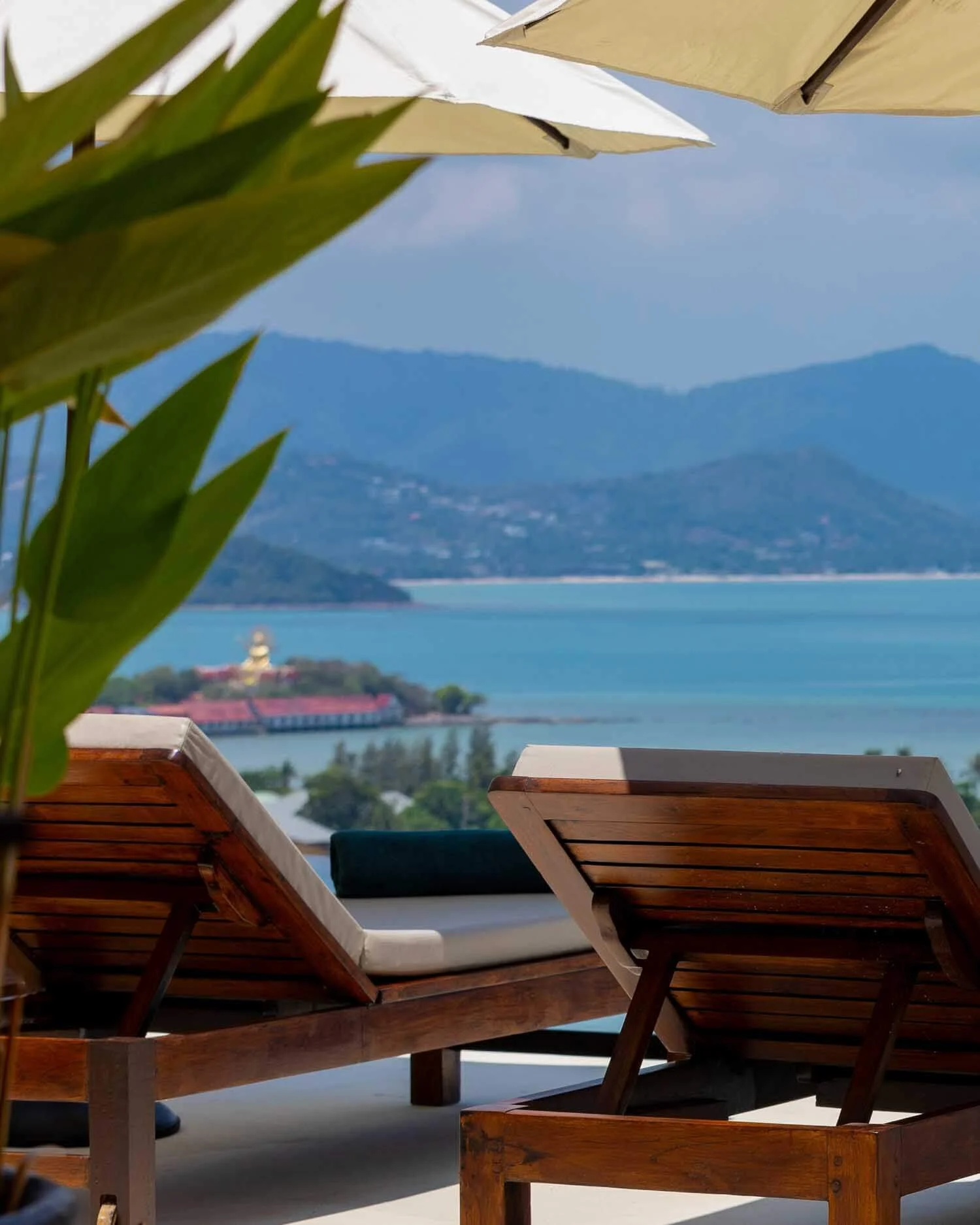 Wooden sun loungers on the terrace of Saensook Villa offering a scenic view of the blue ocean and distant islands in Koh Samui.