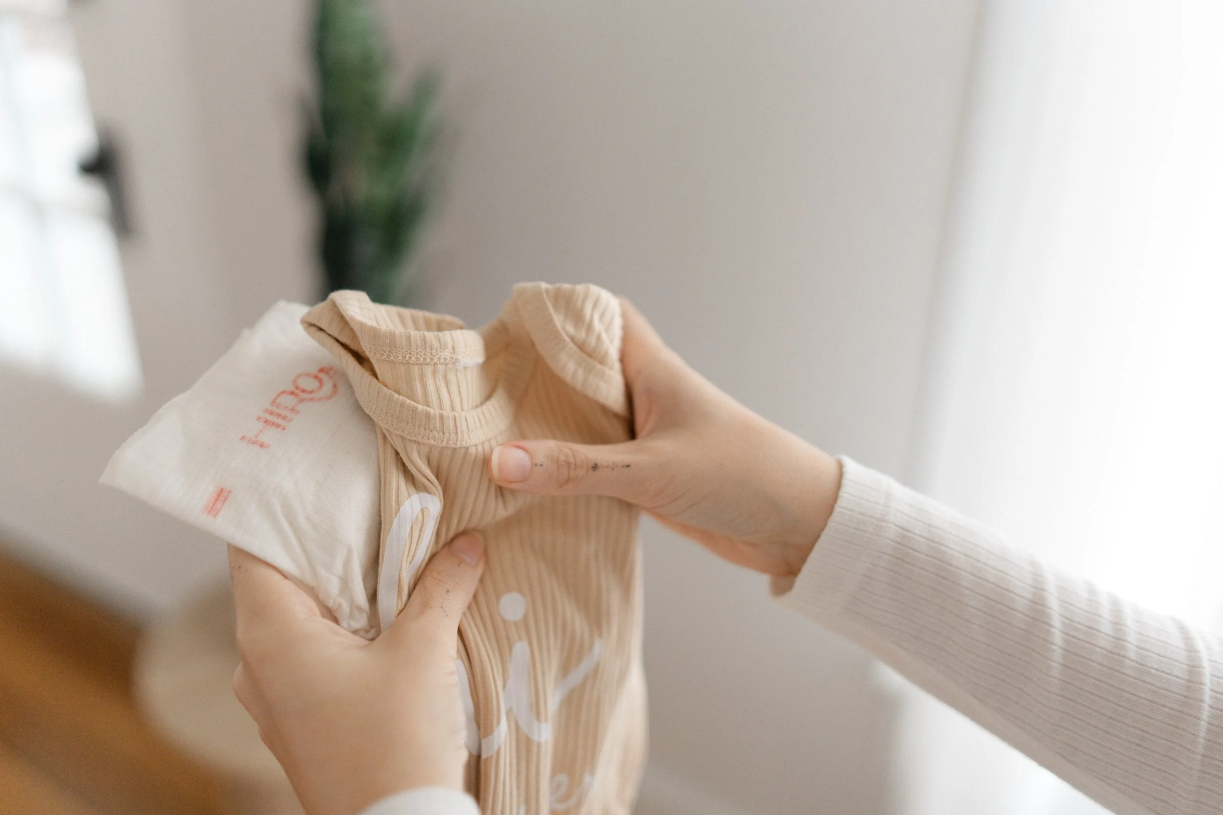 Person holding a beige ribbed baby onesie with a white cloth diaper or garment