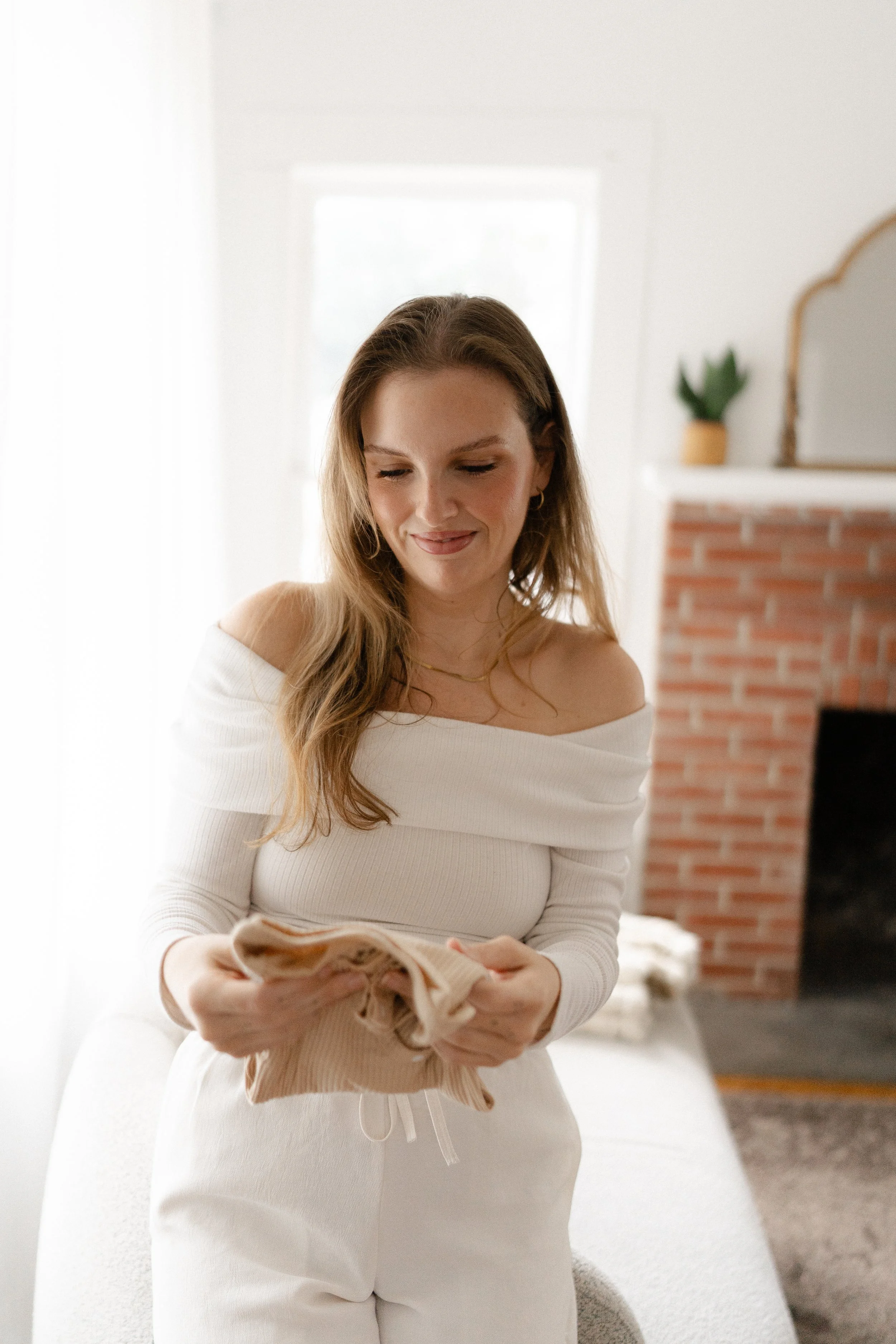 Smiling woman in a white sweater holding a small dog in a bright living room