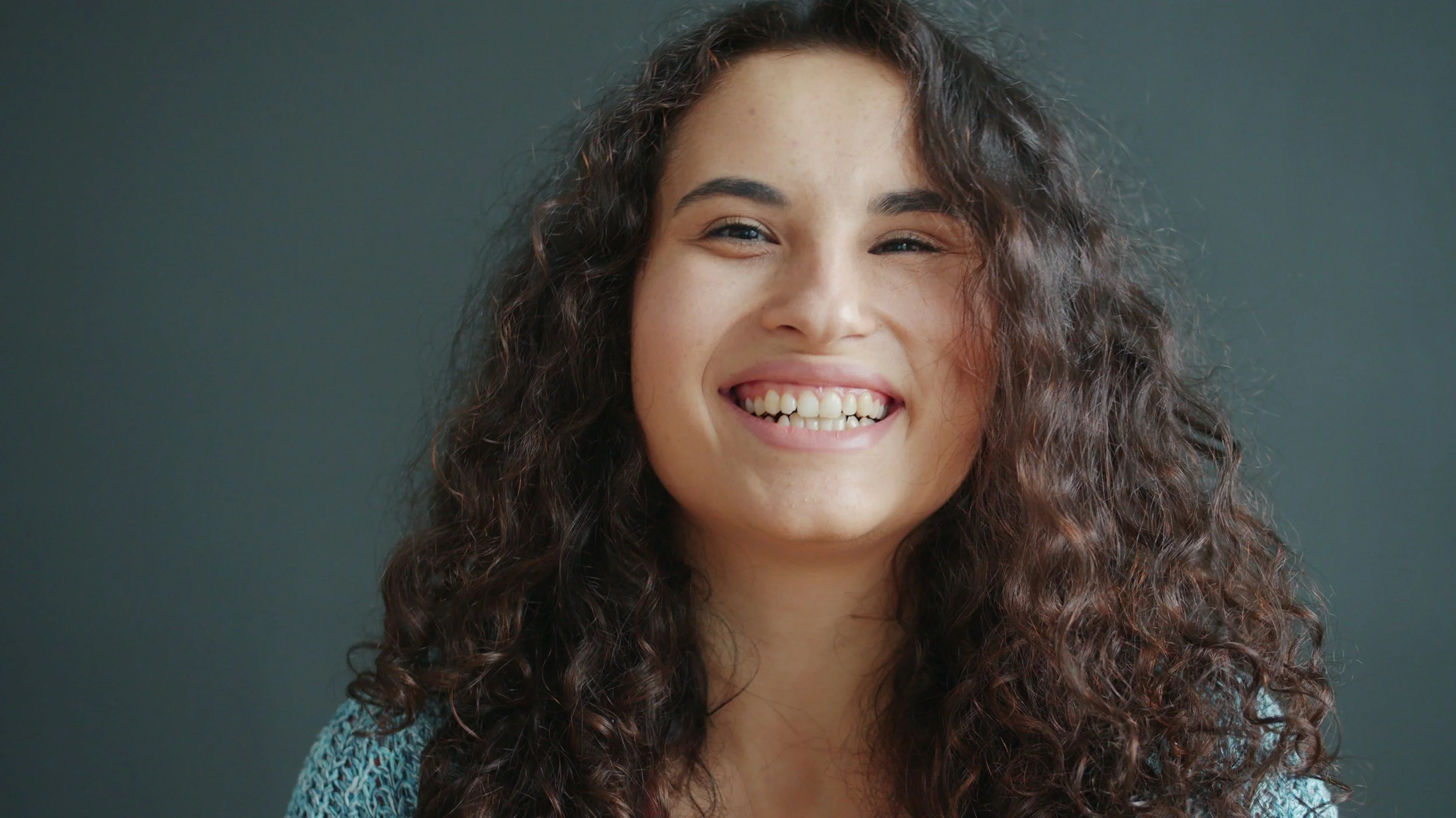 A woman with long, curly brown hair smiling at the camera