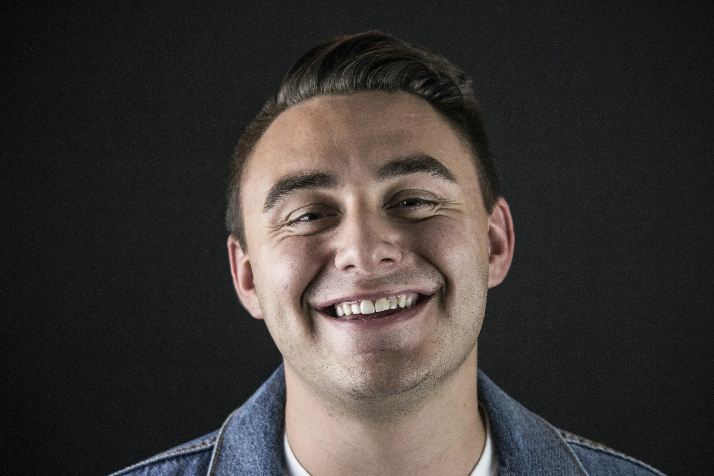 Close-up of a young man smiling against a black background.