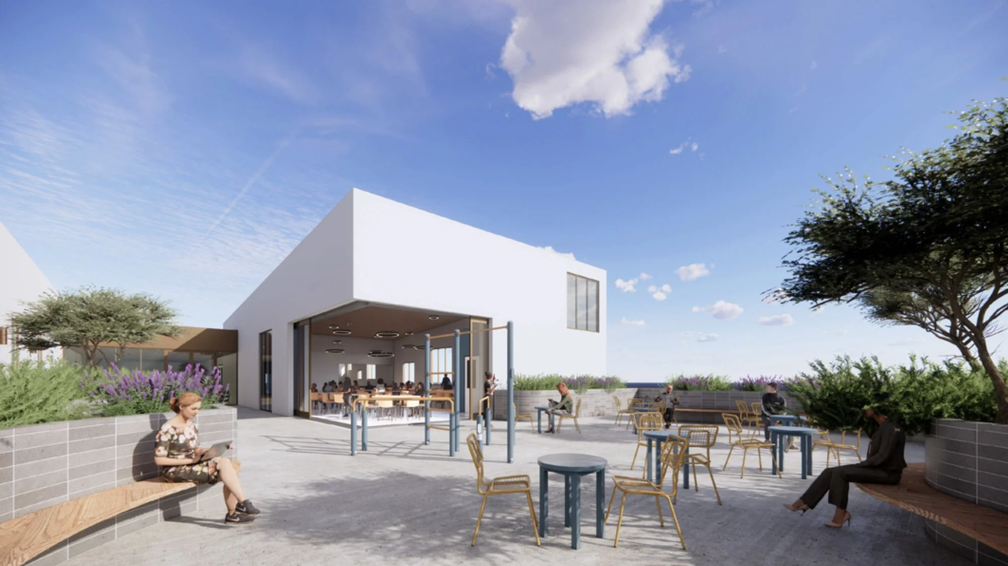 Outdoor seating area with tables, chairs, and people sitting outside near a modern white building under a blue sky with clouds and trees.