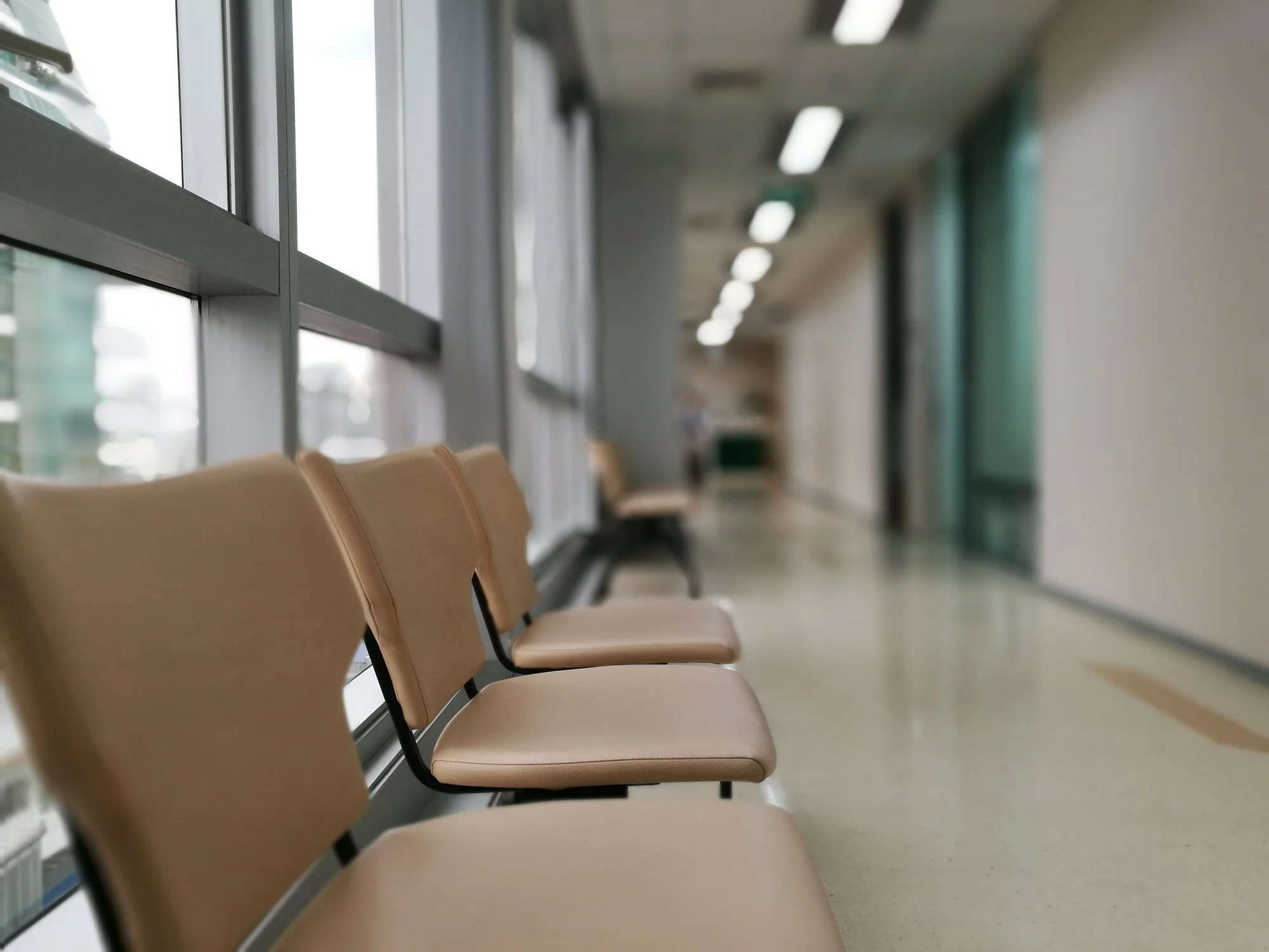 Empty beige chairs in a waiting area with large windows and ceiling lights.