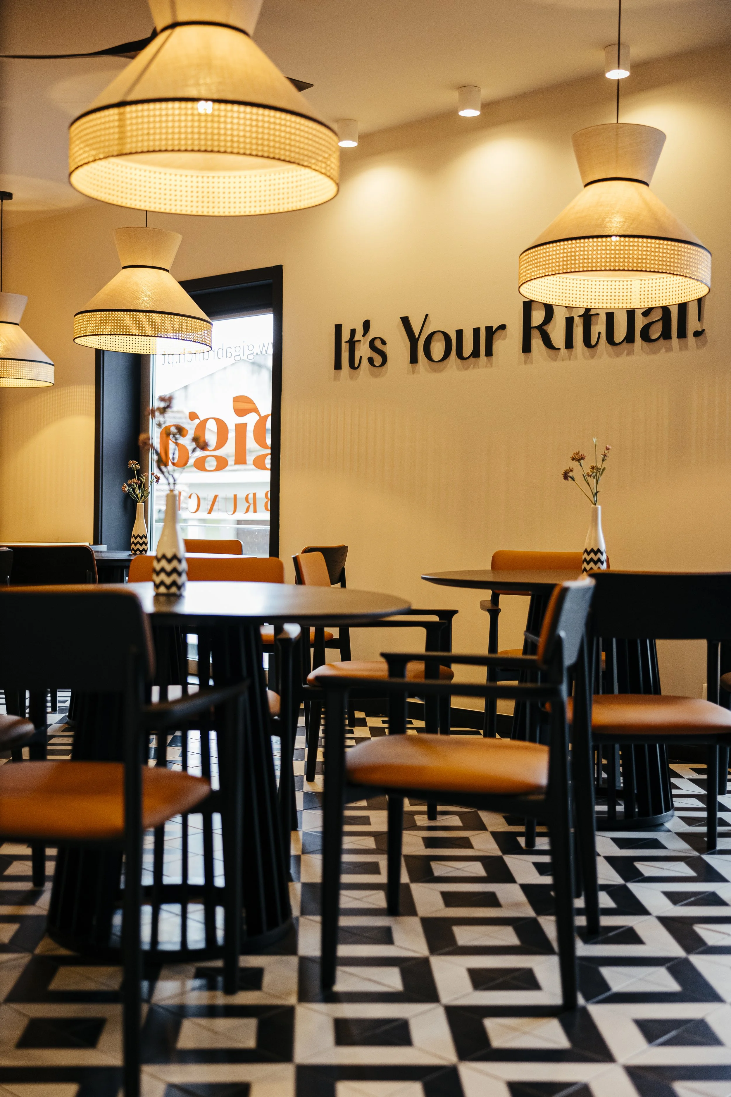 Interior da sala do Giga Brunch, com mesas de madeira e a frase “It’s Your Ritual!” na parede