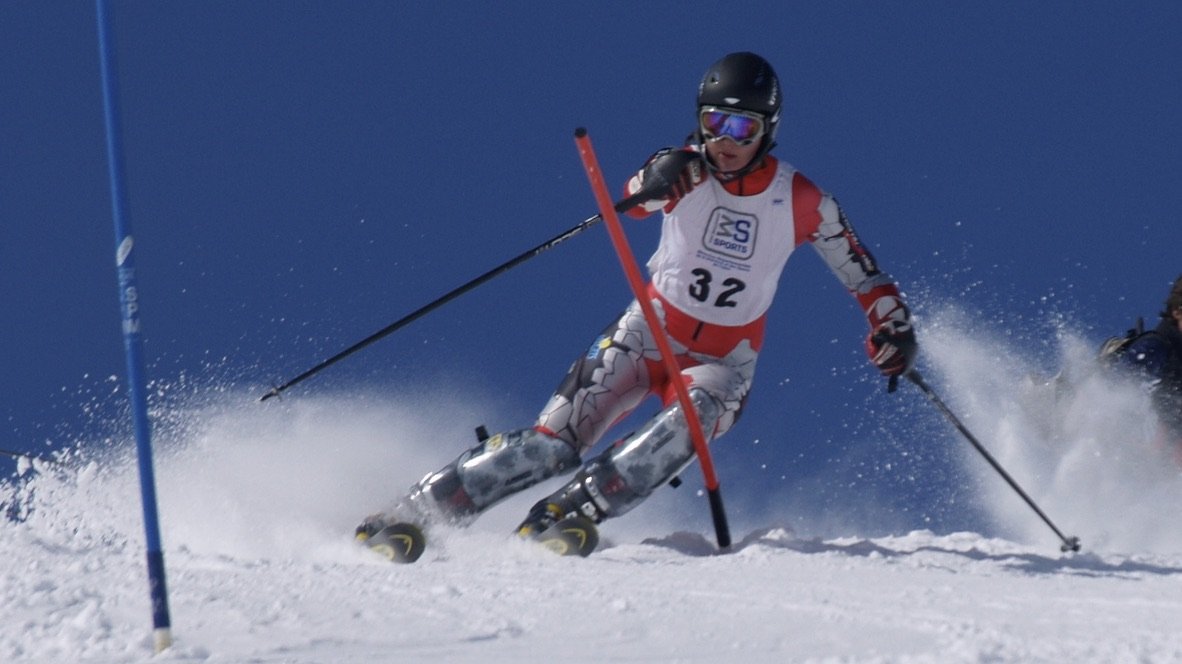 A skier in a red and white racing suit and black helmet skiing around a blue slalom pole during a race in snowy conditions.