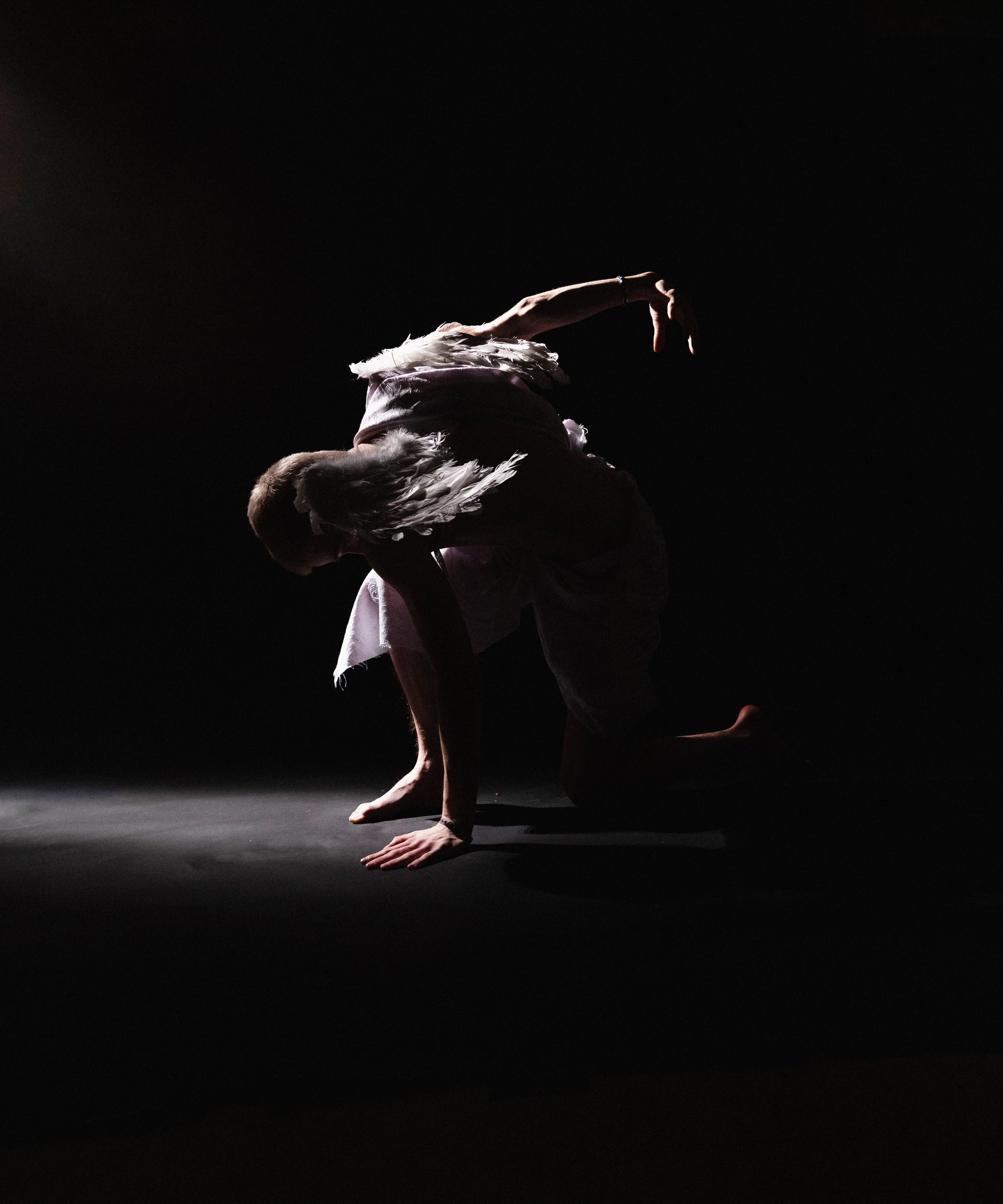 A person with angel wings performing a yoga pose, balancing on their hands with their head down and legs bent, against a black background.