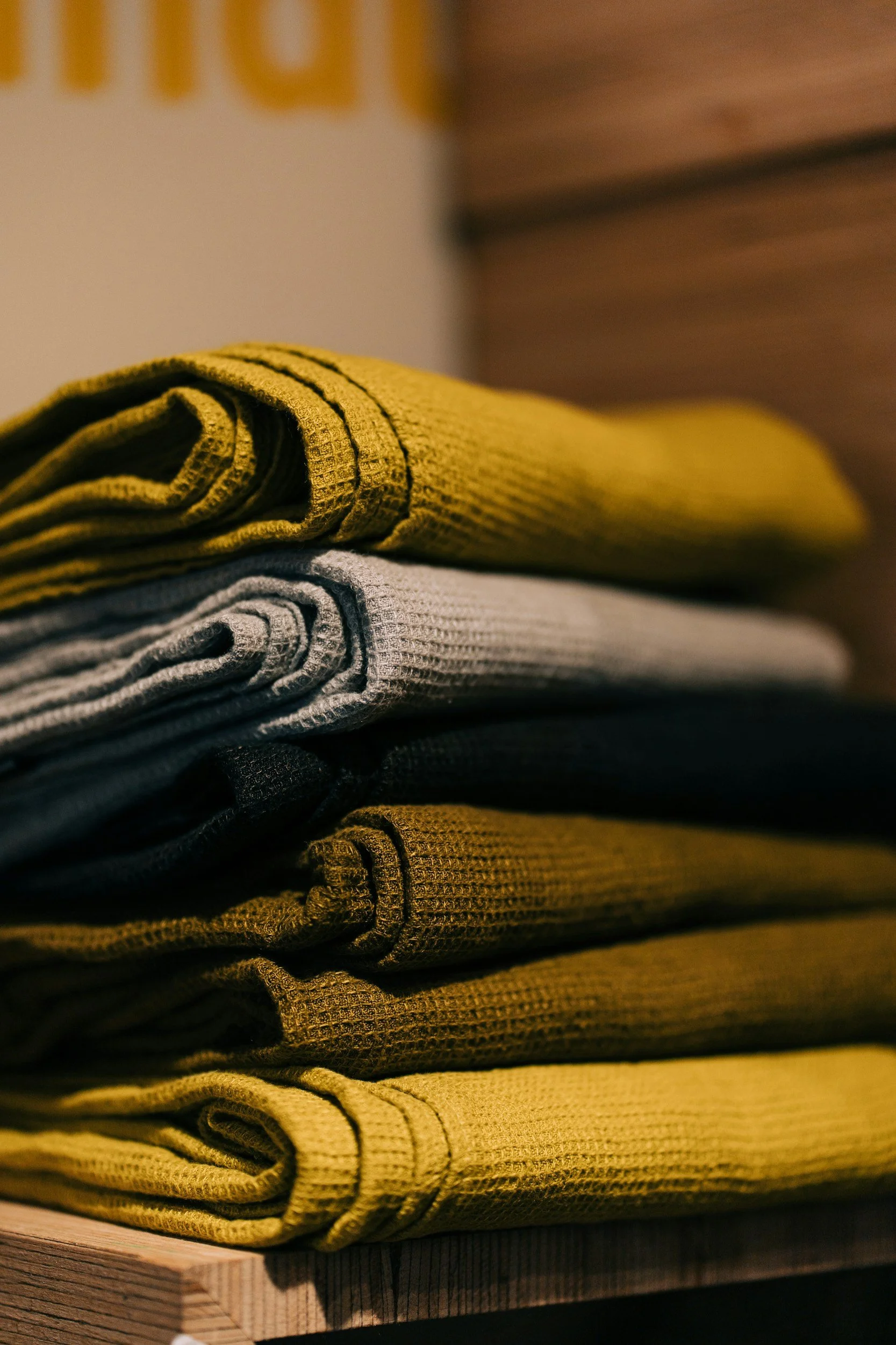 Stacked folded clothes in various colors including yellow, gray, black, and brown on a wooden surface.